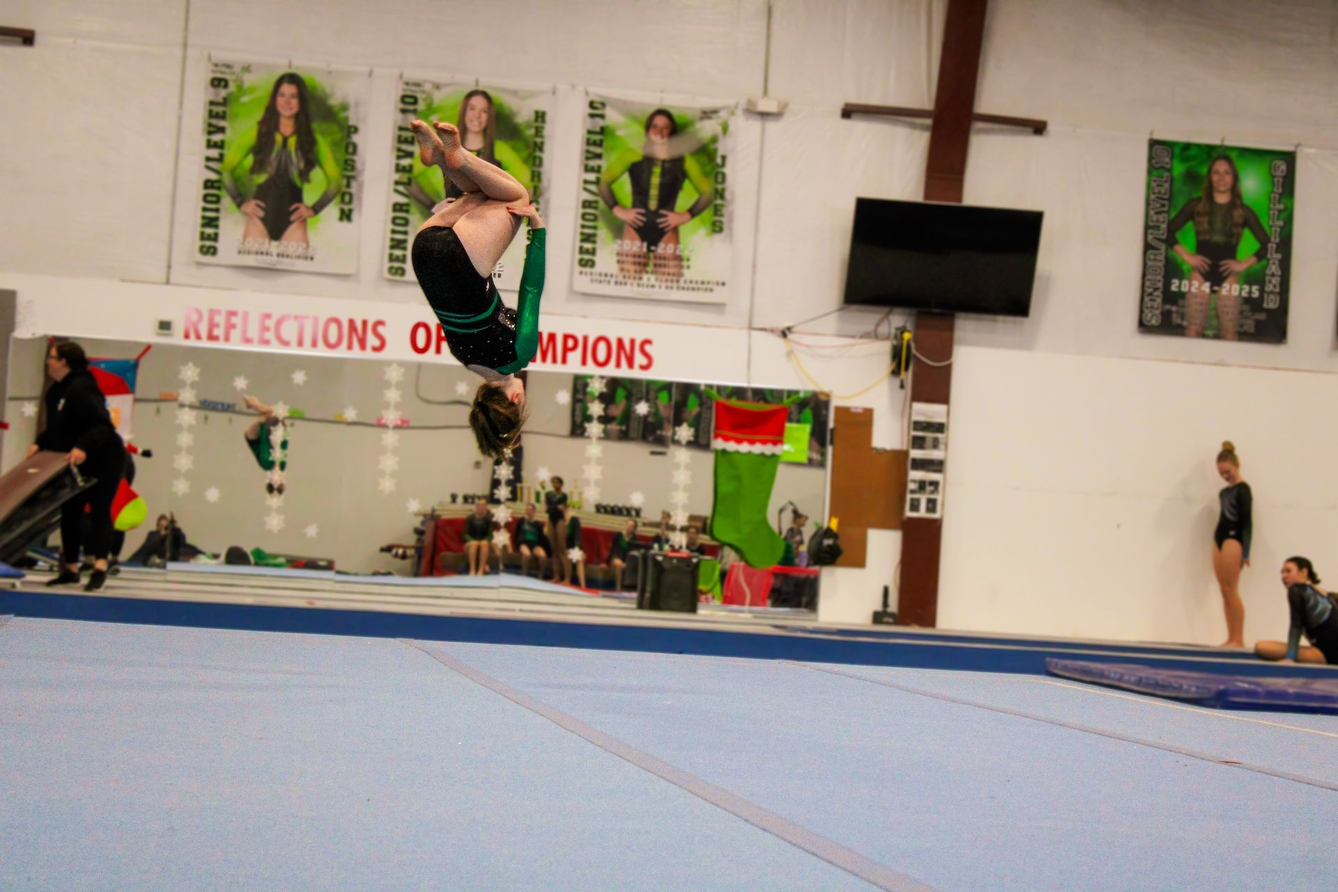 Gymnast midair on vault in a gymnasium during a competition, with judges and spectators in the background
