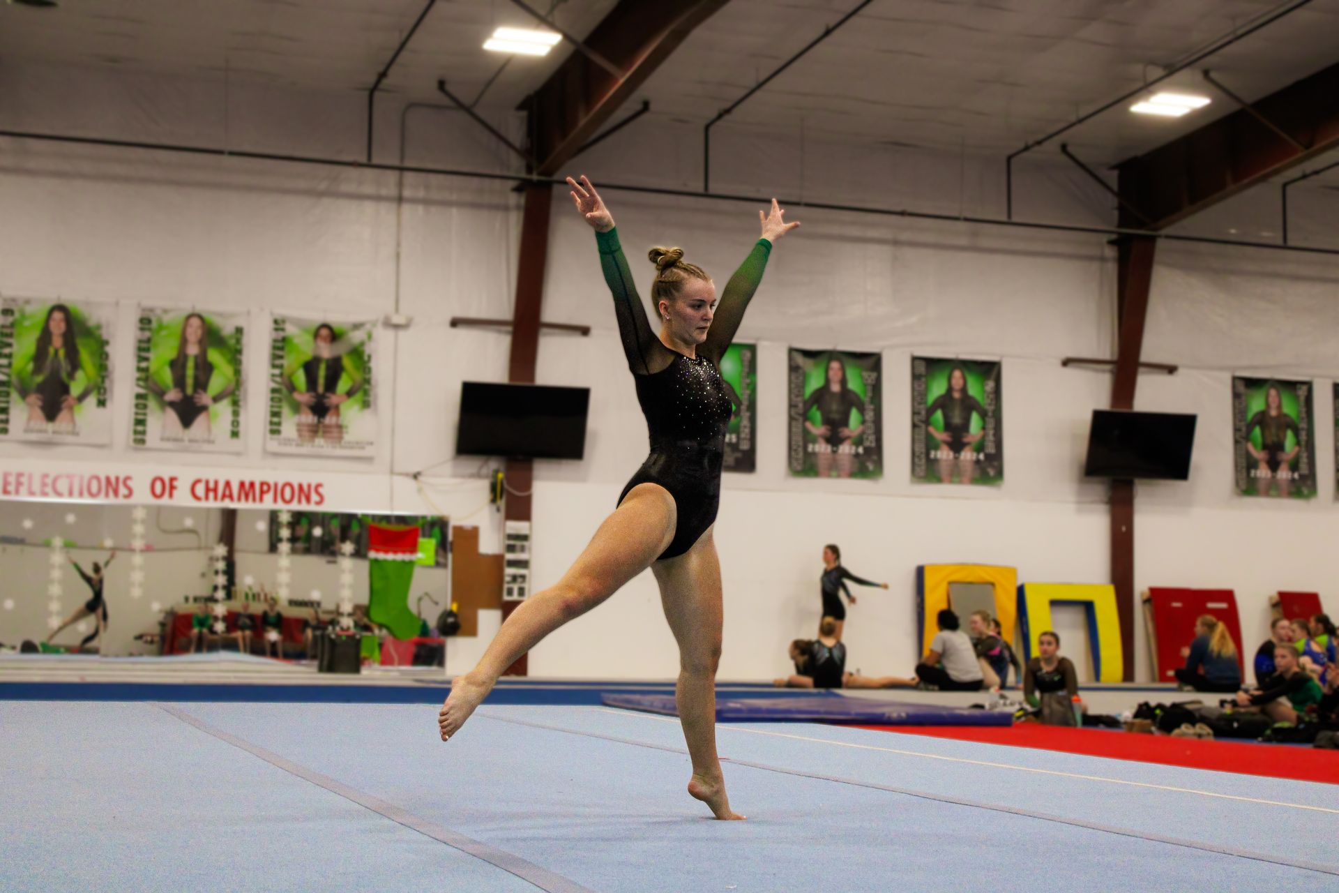 Gymnast in black leotard performing a leap on a balance beam in an indoor gymnasium