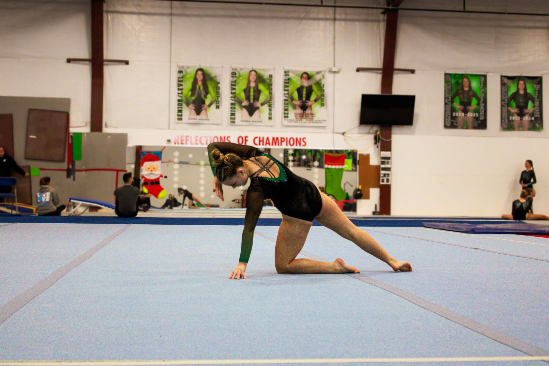 Gymnast in black and gold performs a floor routine pose in an indoor gymnasium.