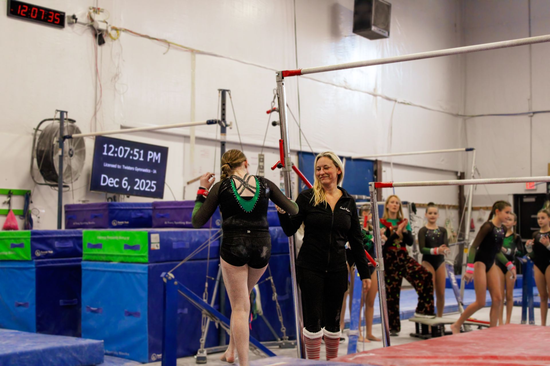 Gymnastics team on the uneven bars in a gym, with athletes in black leotards and coaches nearby