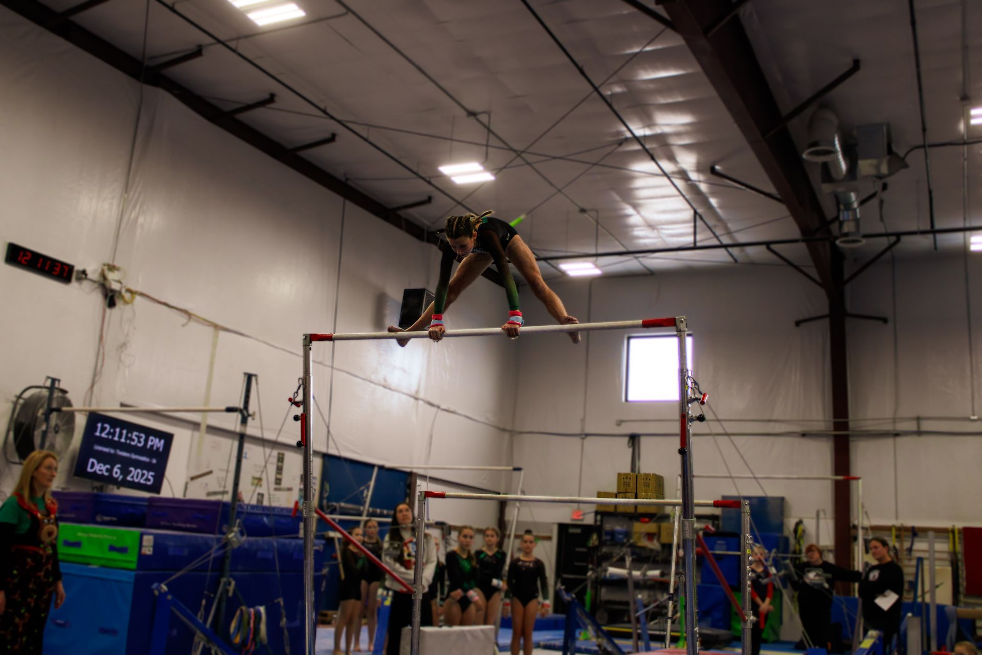 Gymnast on high bar mid-inversion above spotting mats in an indoor training gym