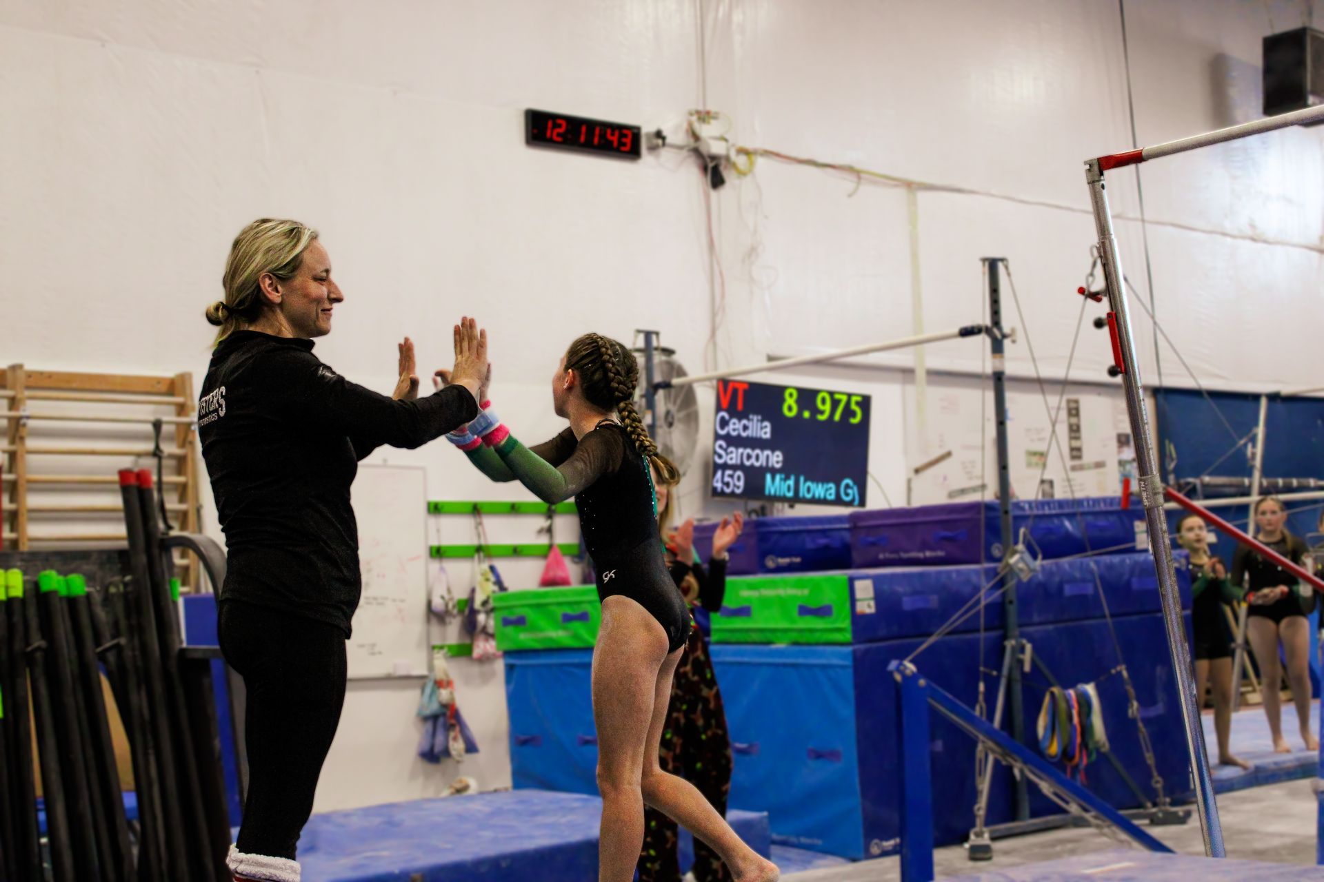 Gymnast and coach high-five beside the uneven bars in an indoor gym.