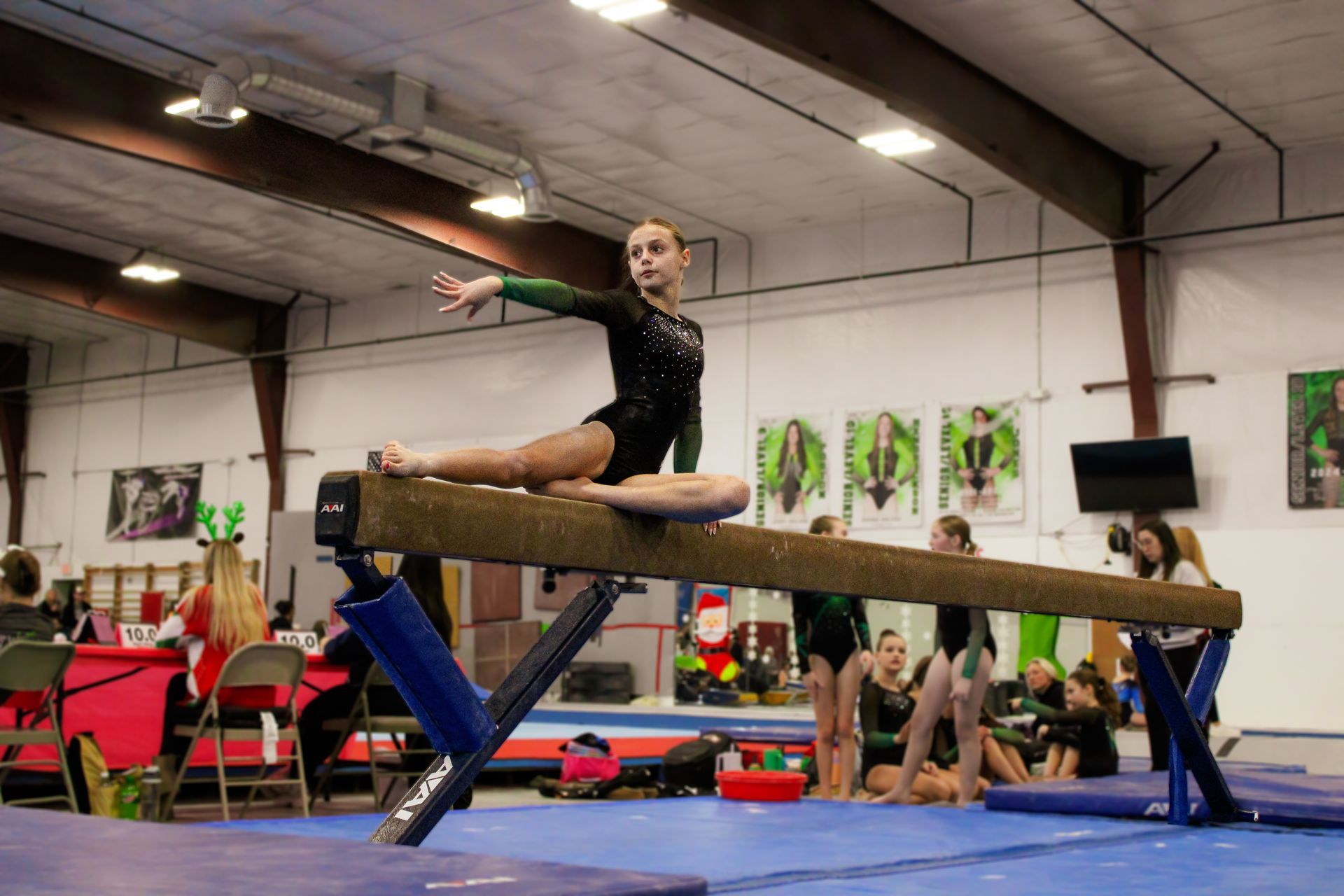 Gymnast balancing on a beam in a gym, with legs extended and spectators in the background.