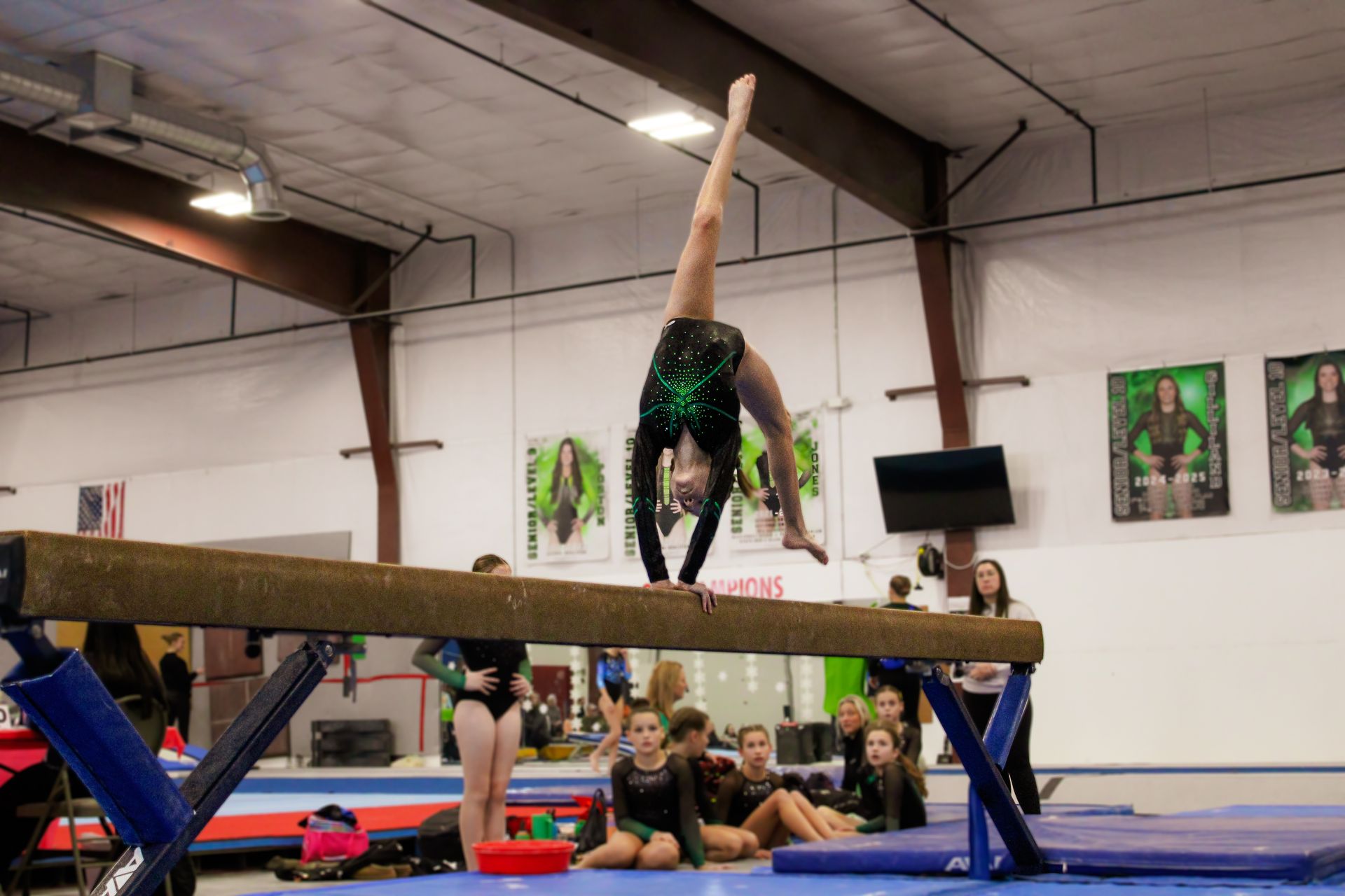 Gymnast balancing on a beam in an indoor training gym, upside down in a handstand.