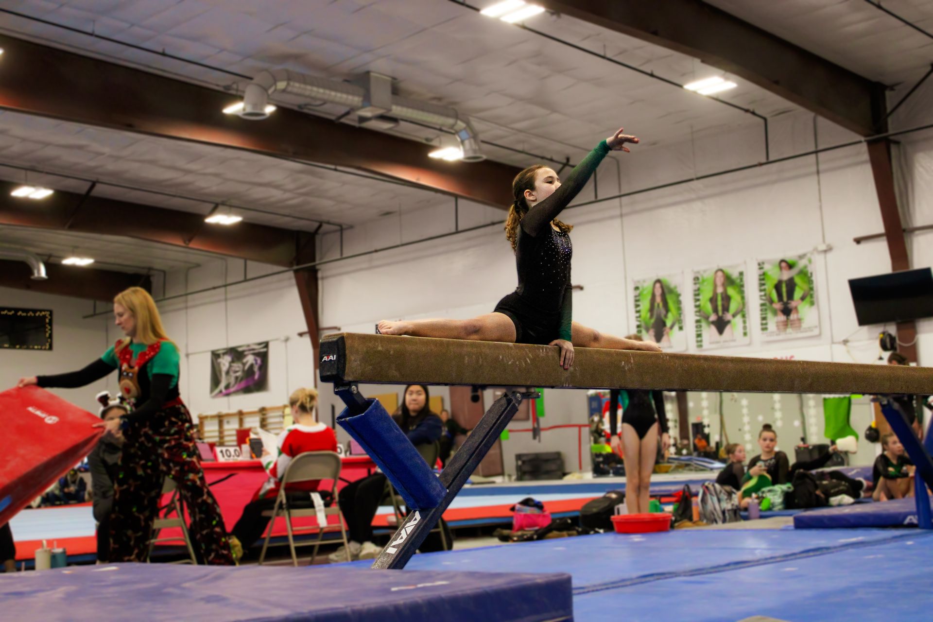 Gymnast balancing on a beam in a gym, with arms raised and teammates nearby