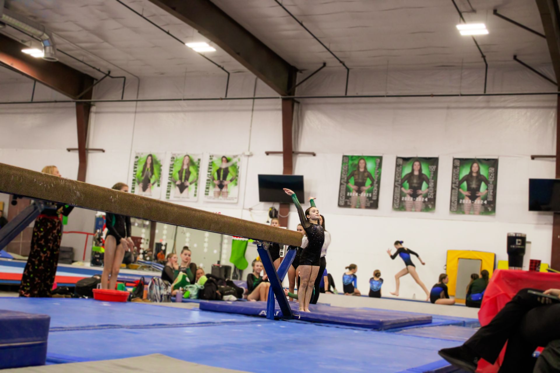 Gymnastics training in a gym, with a balance beam and athletes on blue mats.