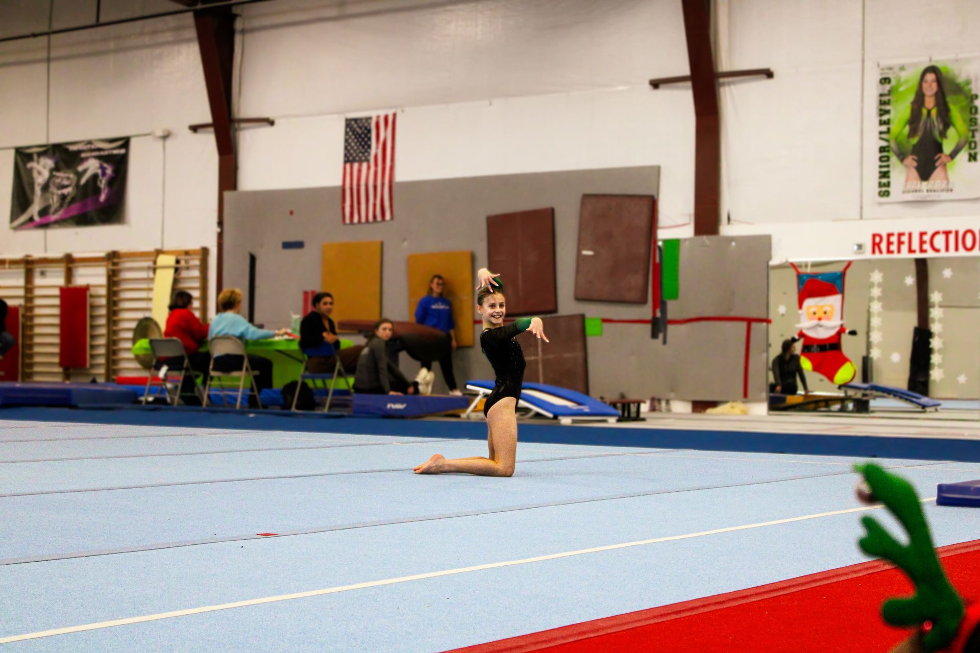 Gymnast kneeling on a blue mat in a gymnasium during a routine.
