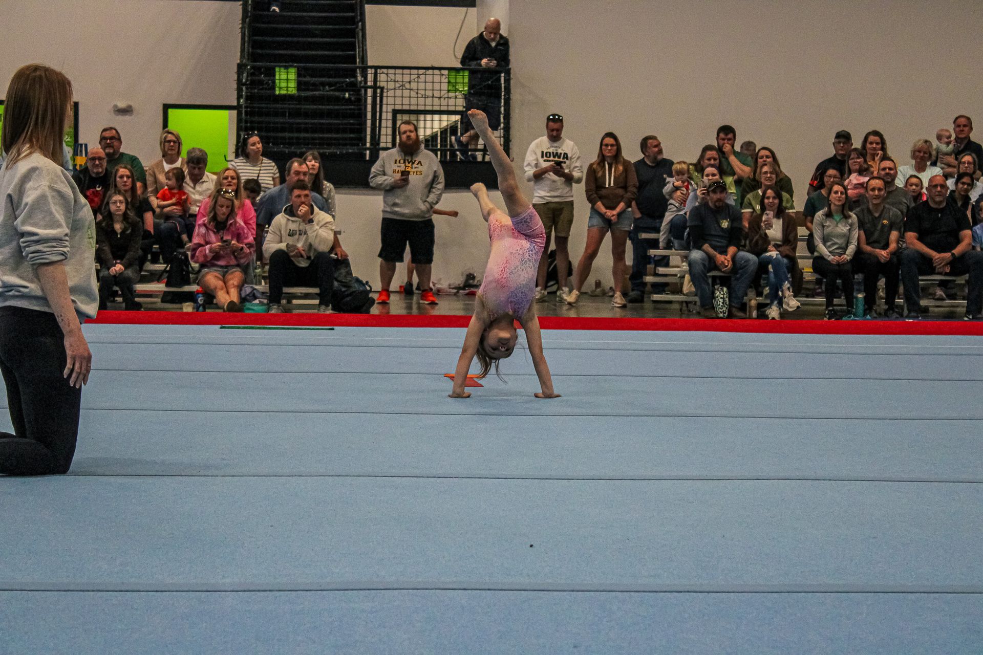 Gymnast doing a handstand on a blue mat at a competition with spectators in the background