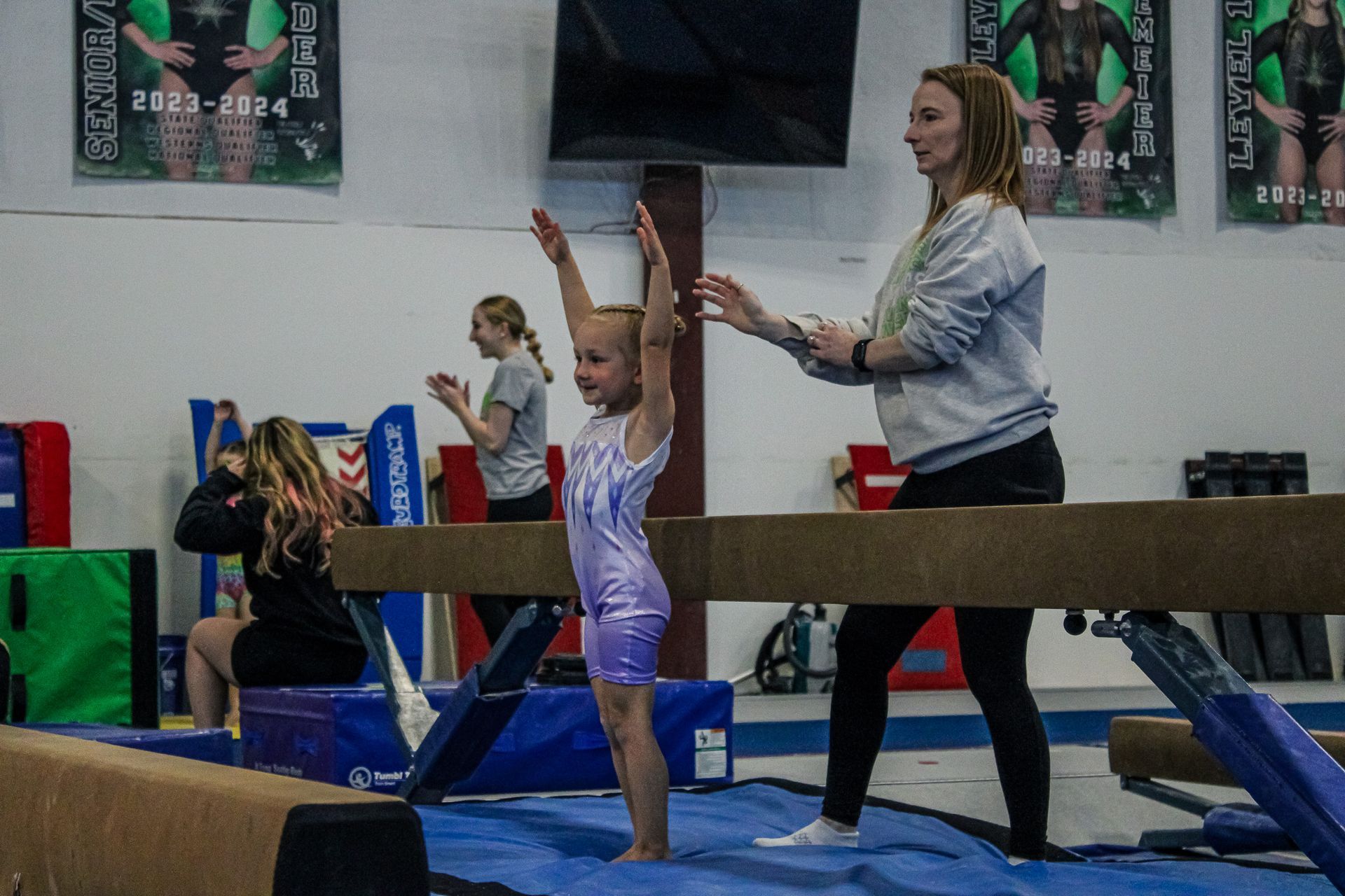Gymnastics class: children practice on balance beams while a coach spots them in a gym.