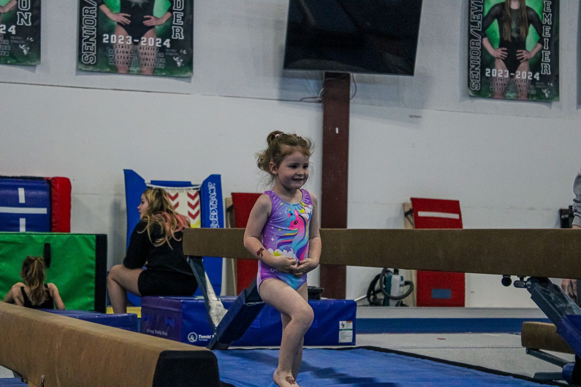 Child in a colorful leotard walking on a balance beam in a gymnasium
