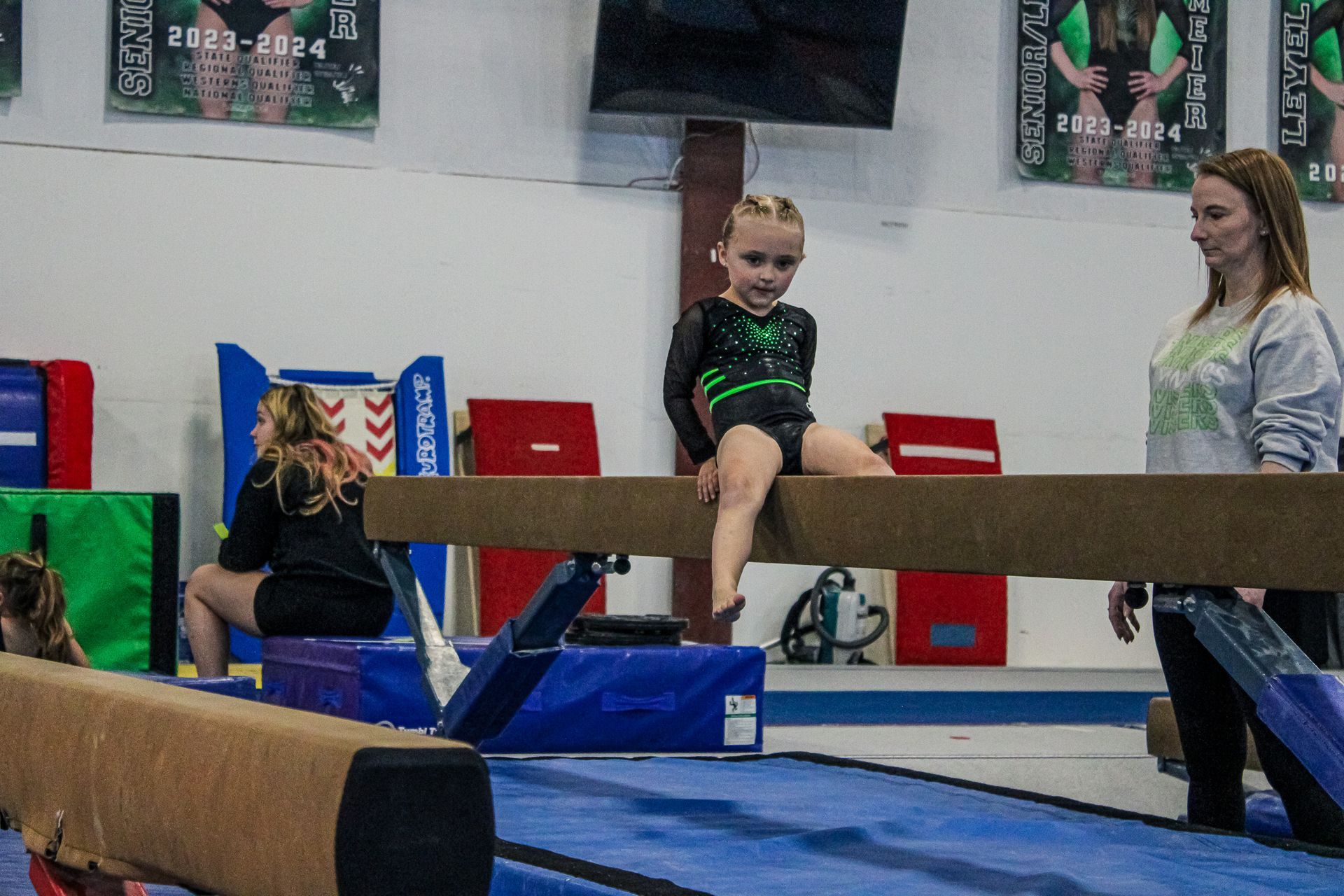 Child balancing on a beam in a gymnastics gym while a coach stands nearby
