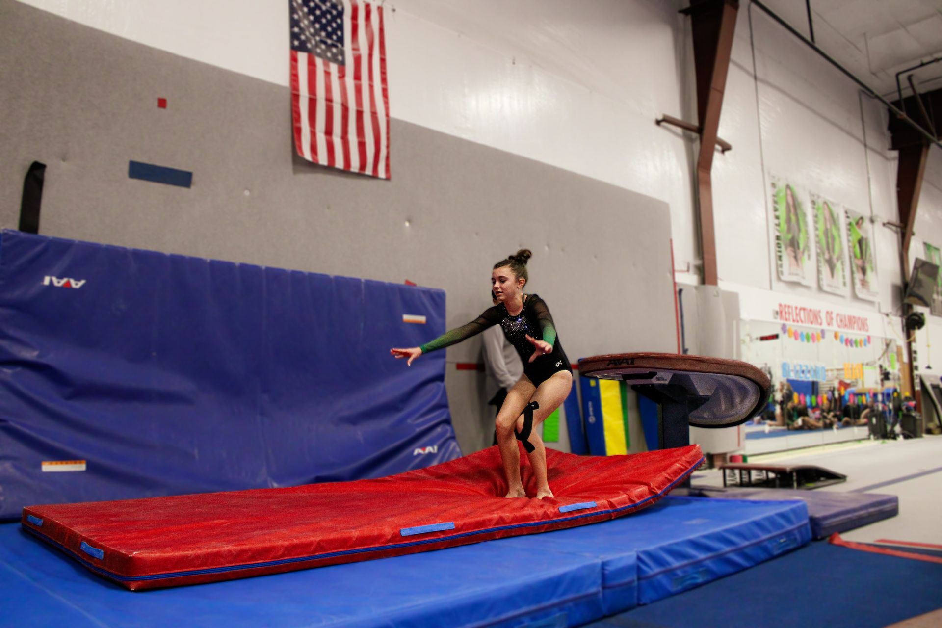 Gymnast practicing a jump onto a red mat in an indoor gymnasium