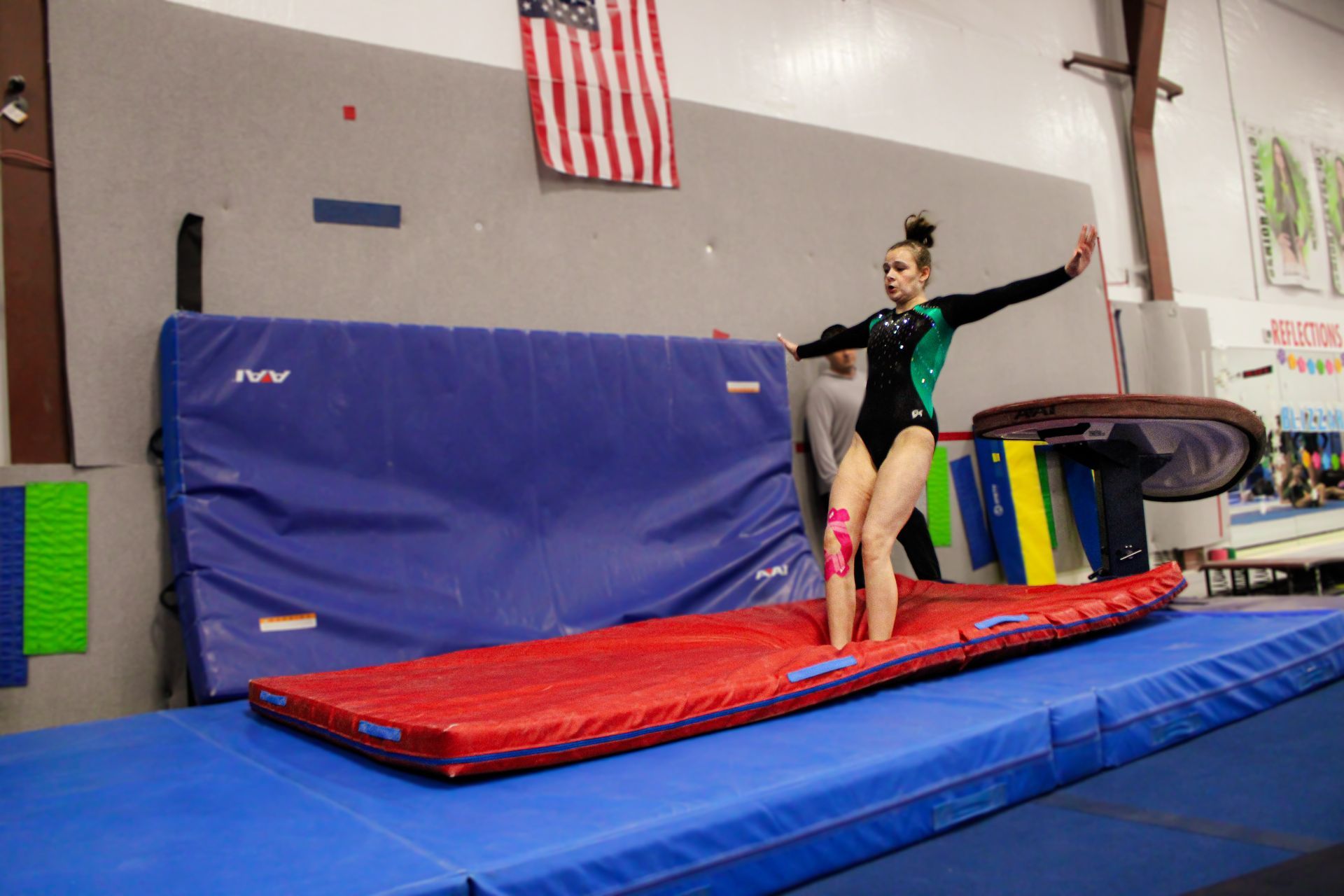 Gymnast balancing on a red mat in a gym, with arms outstretched near a blue foam pit.