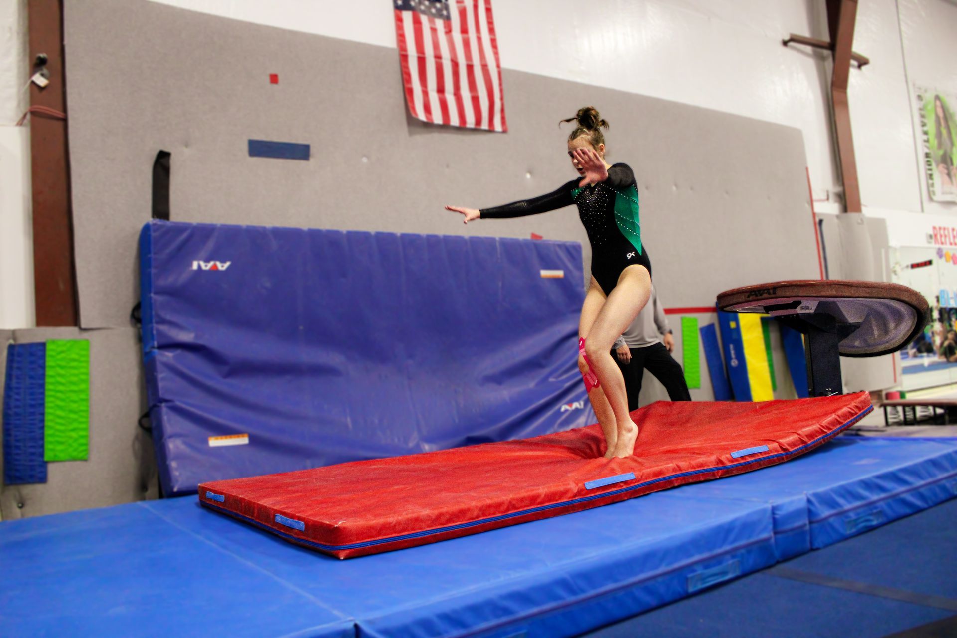 Gymnast balancing on a red mat in a gym, arms outstretched near a padded wall