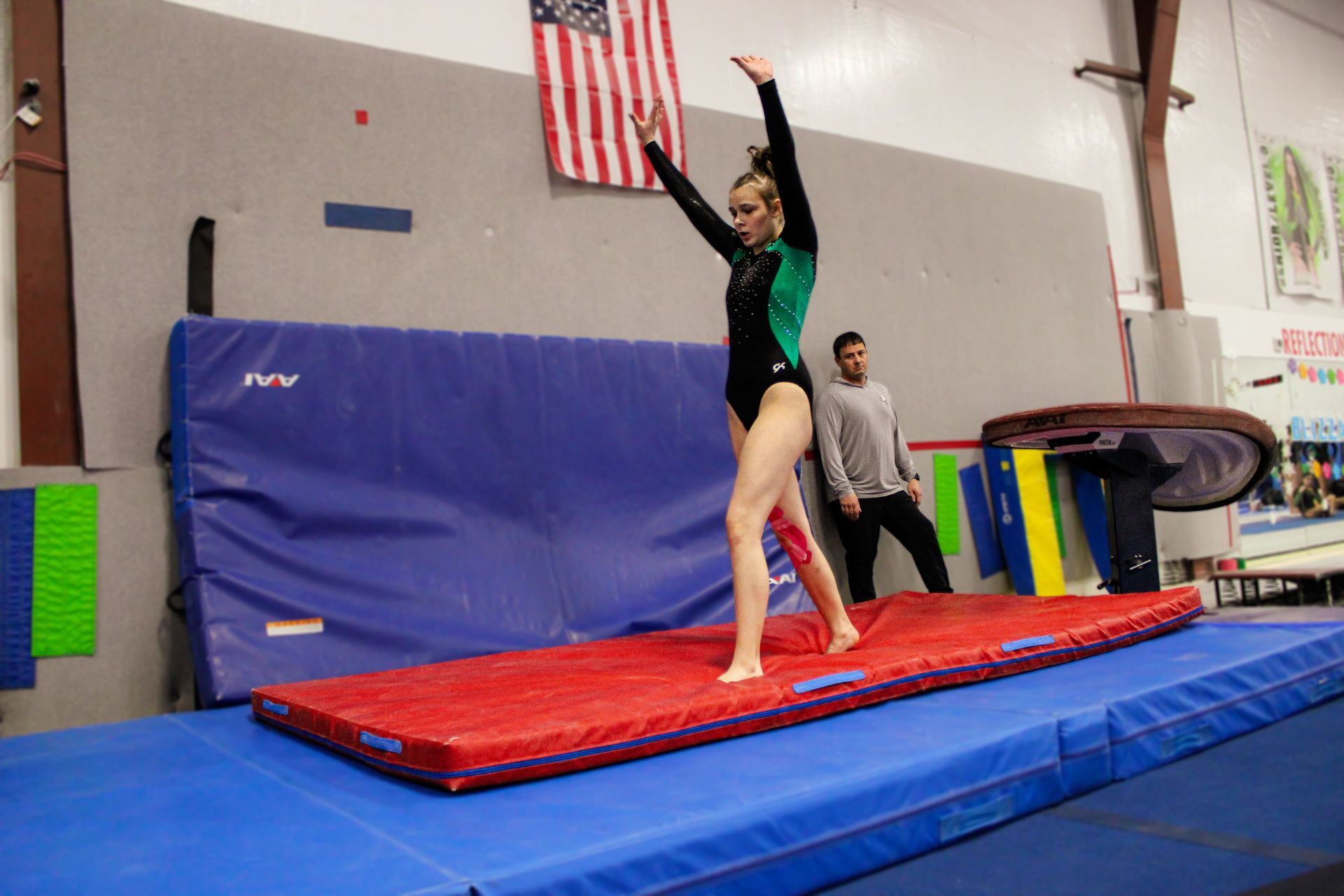 Gymnast balancing on a blue and red mat in an indoor gym, arms raised overhead