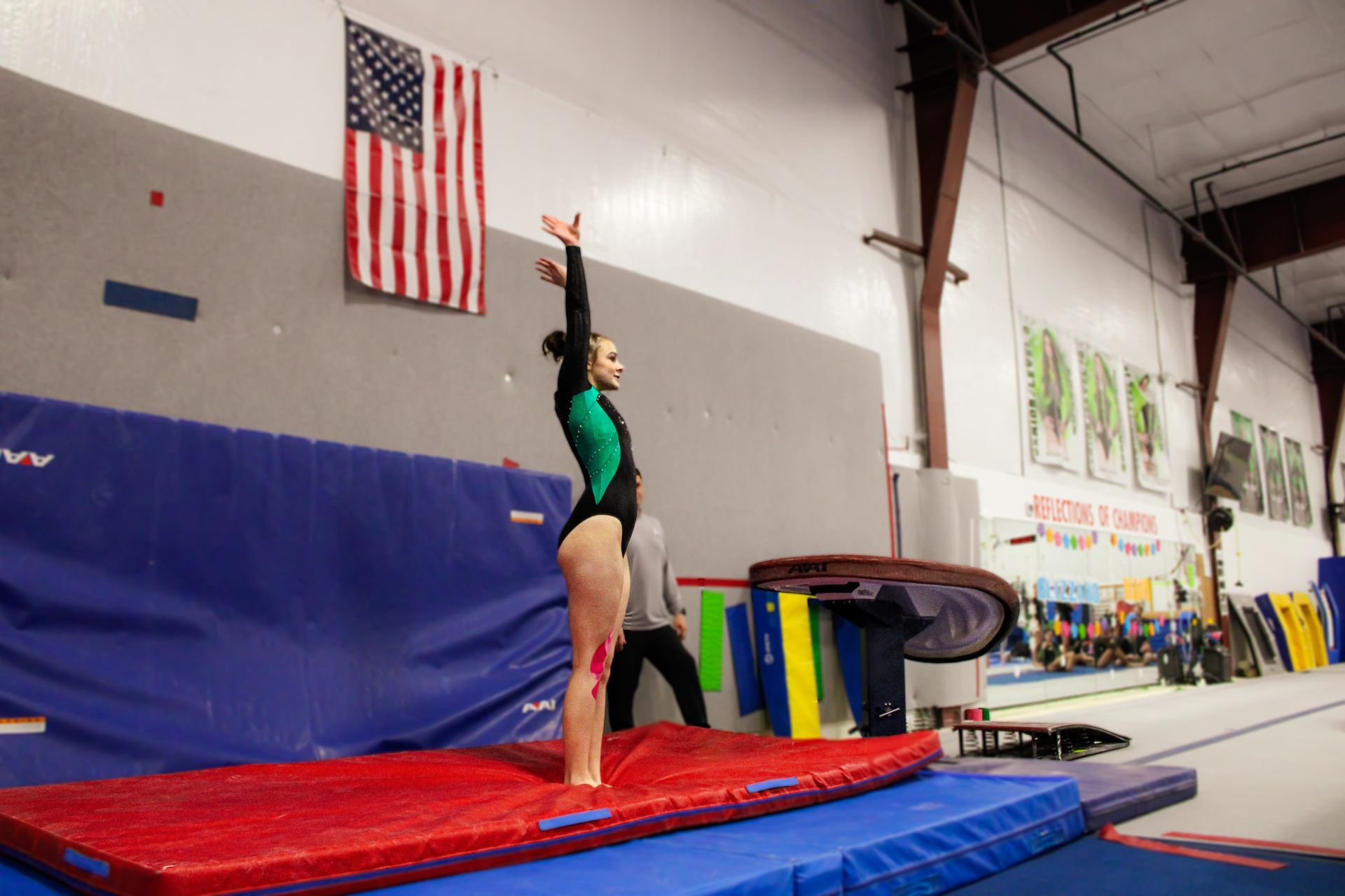 Gymnast standing on a red mat with arms raised in an indoor gymnasium