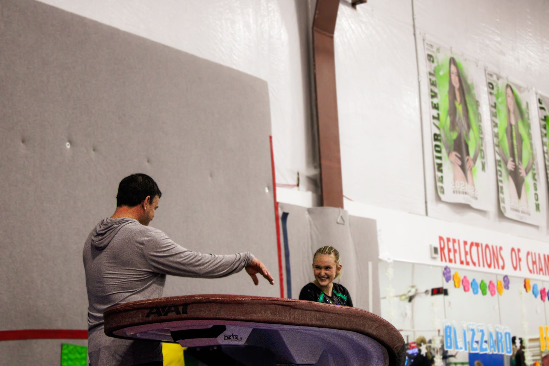 Two people stand by a large purple circular trampoline in a gym or event hall.