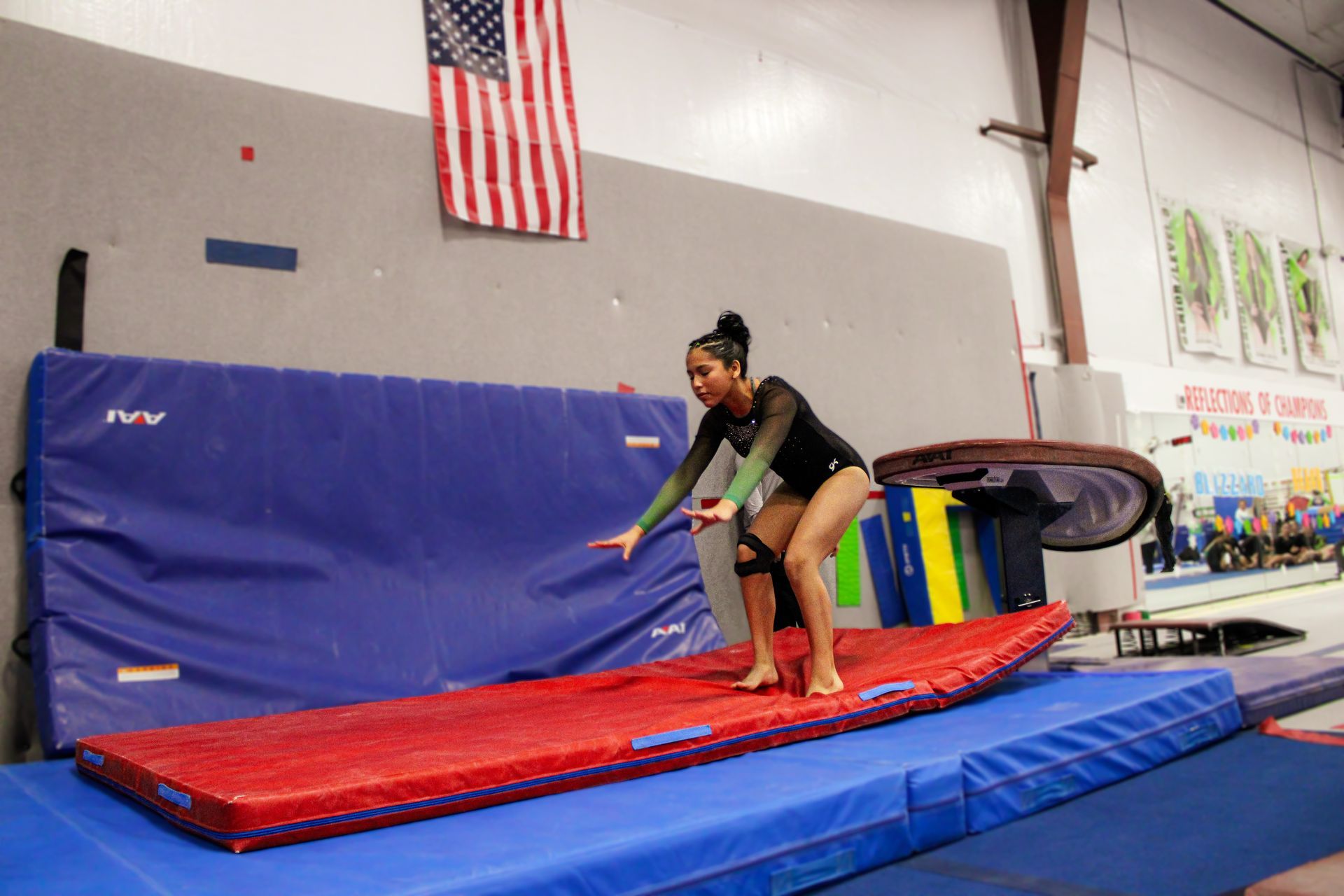Gymnast on a red mat preparing to jump onto a blue crash mat in a gymnasium