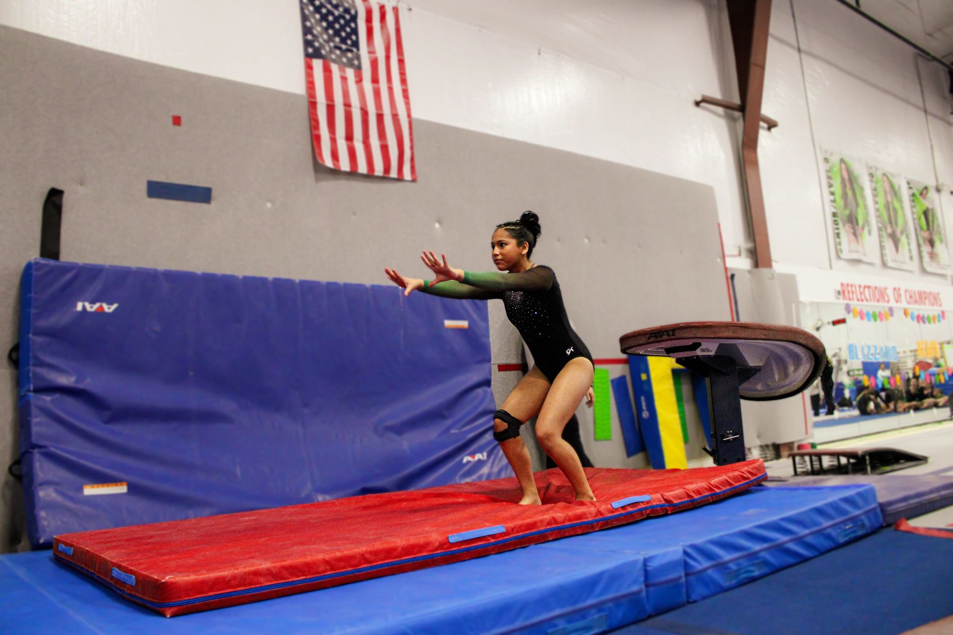 Gymnast balancing on a red beam over blue mats in an indoor gymnasium