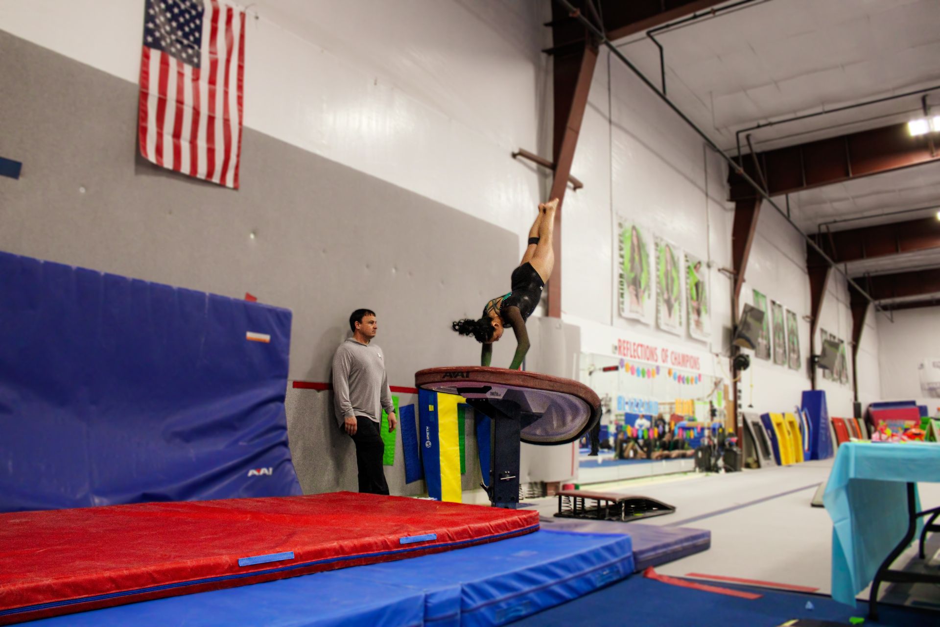 Gymnast balancing upside down on a high bar over mats in a gym