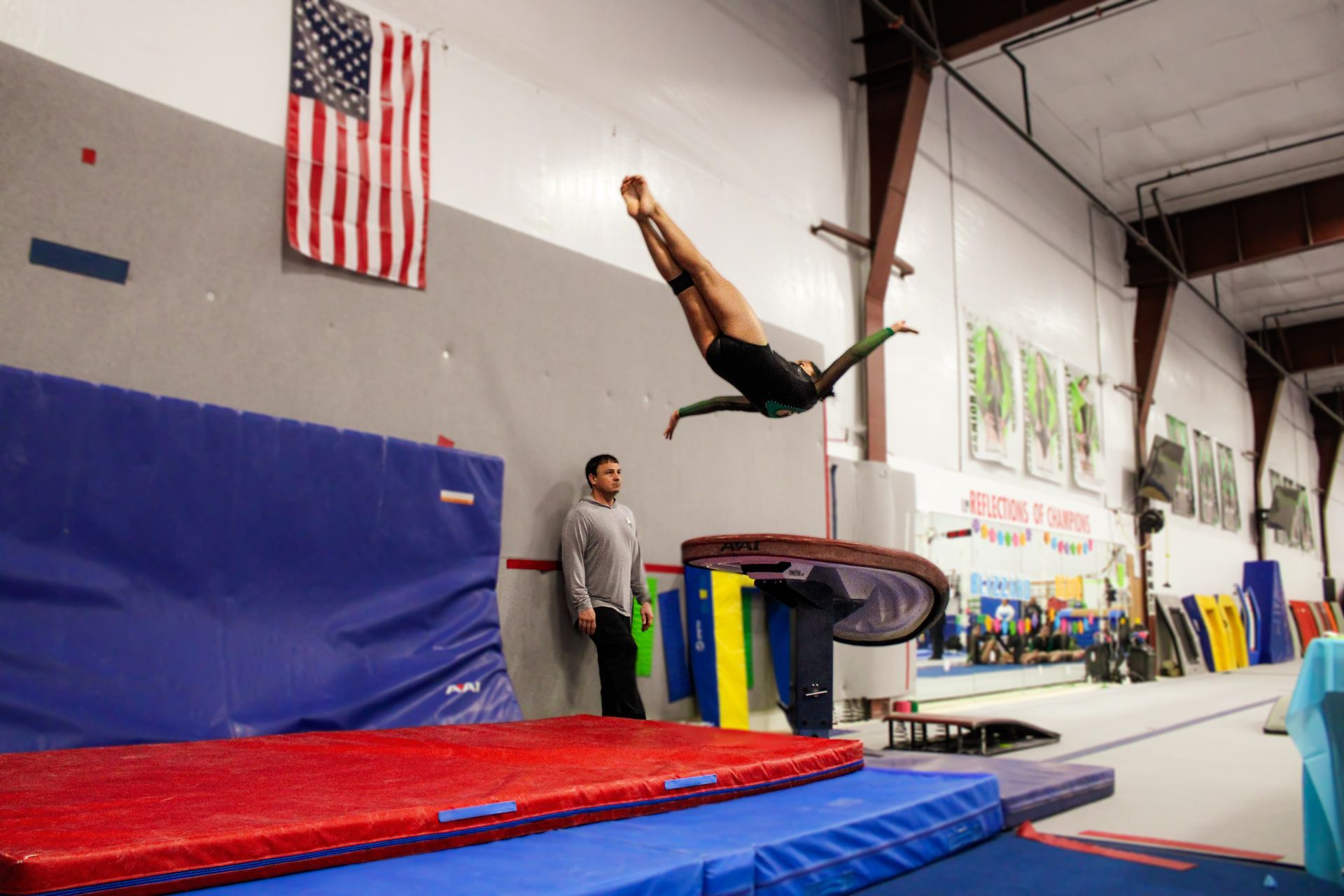 Gymnast flipping over a foam pit in an indoor training gym with red and blue mats.