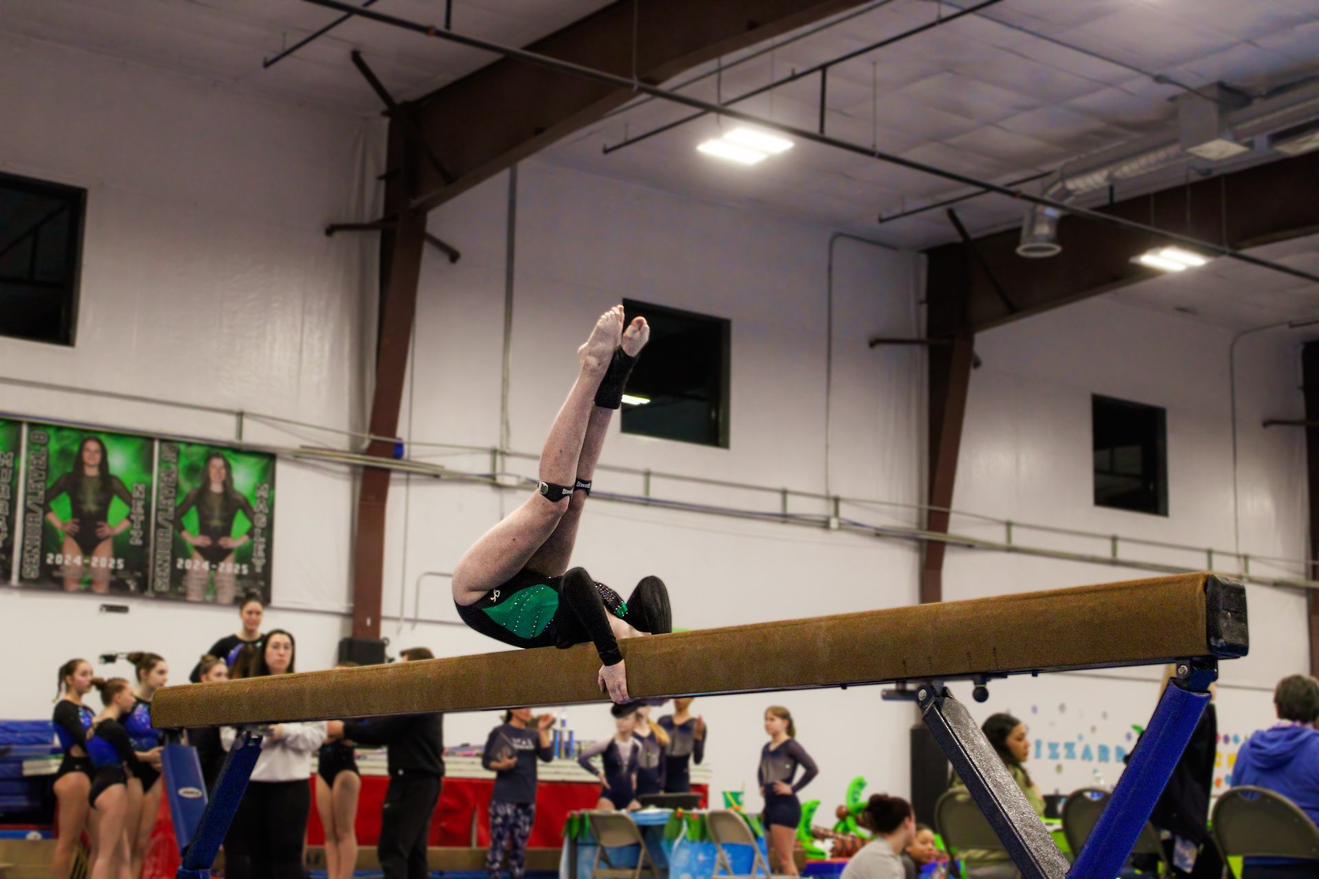 Gymnast mid-flip over a balance beam in a gymnasium competition, with spectators in the background