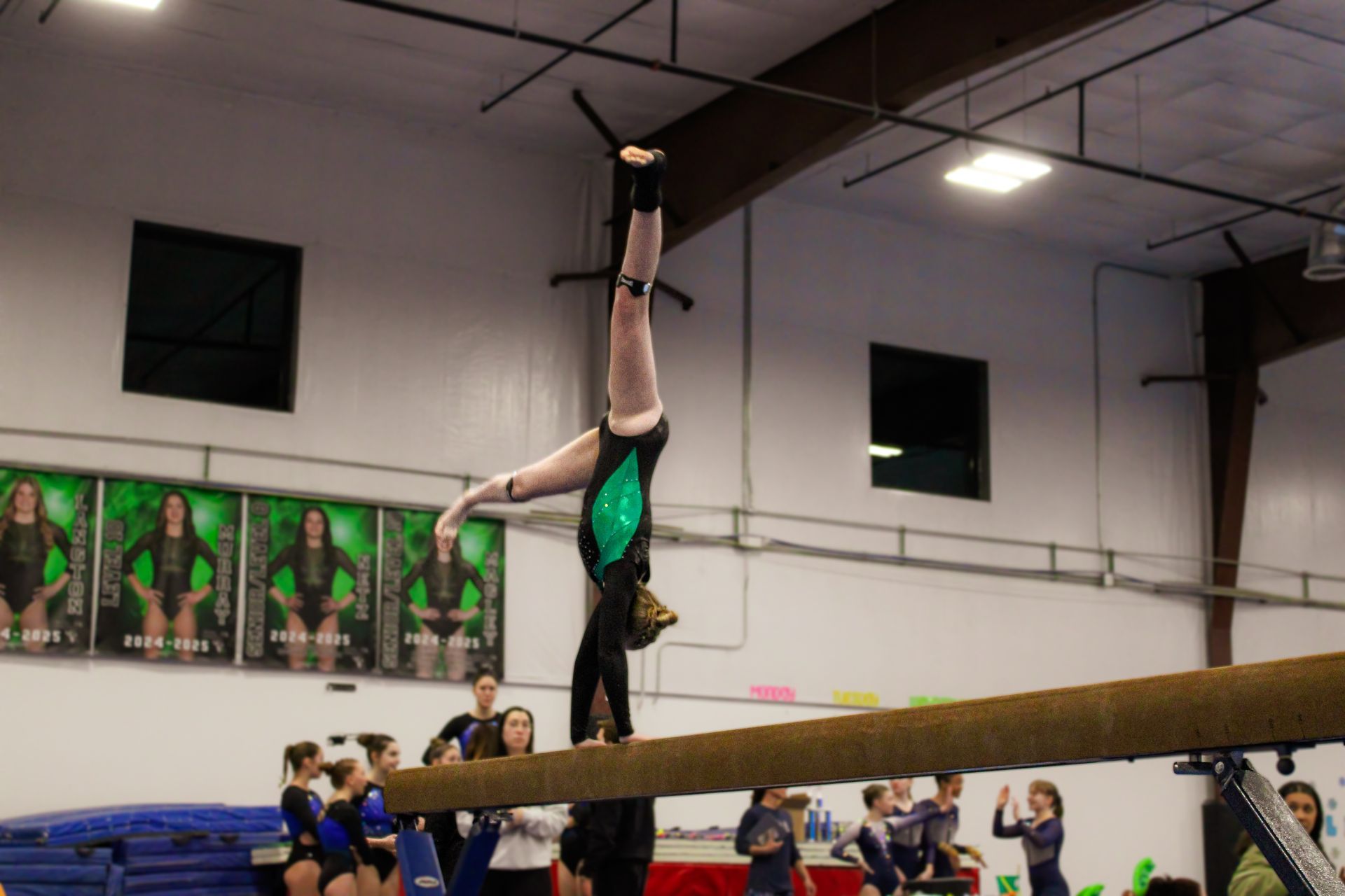 Gymnast in a handstand on a balance beam in a gymnasium competition.