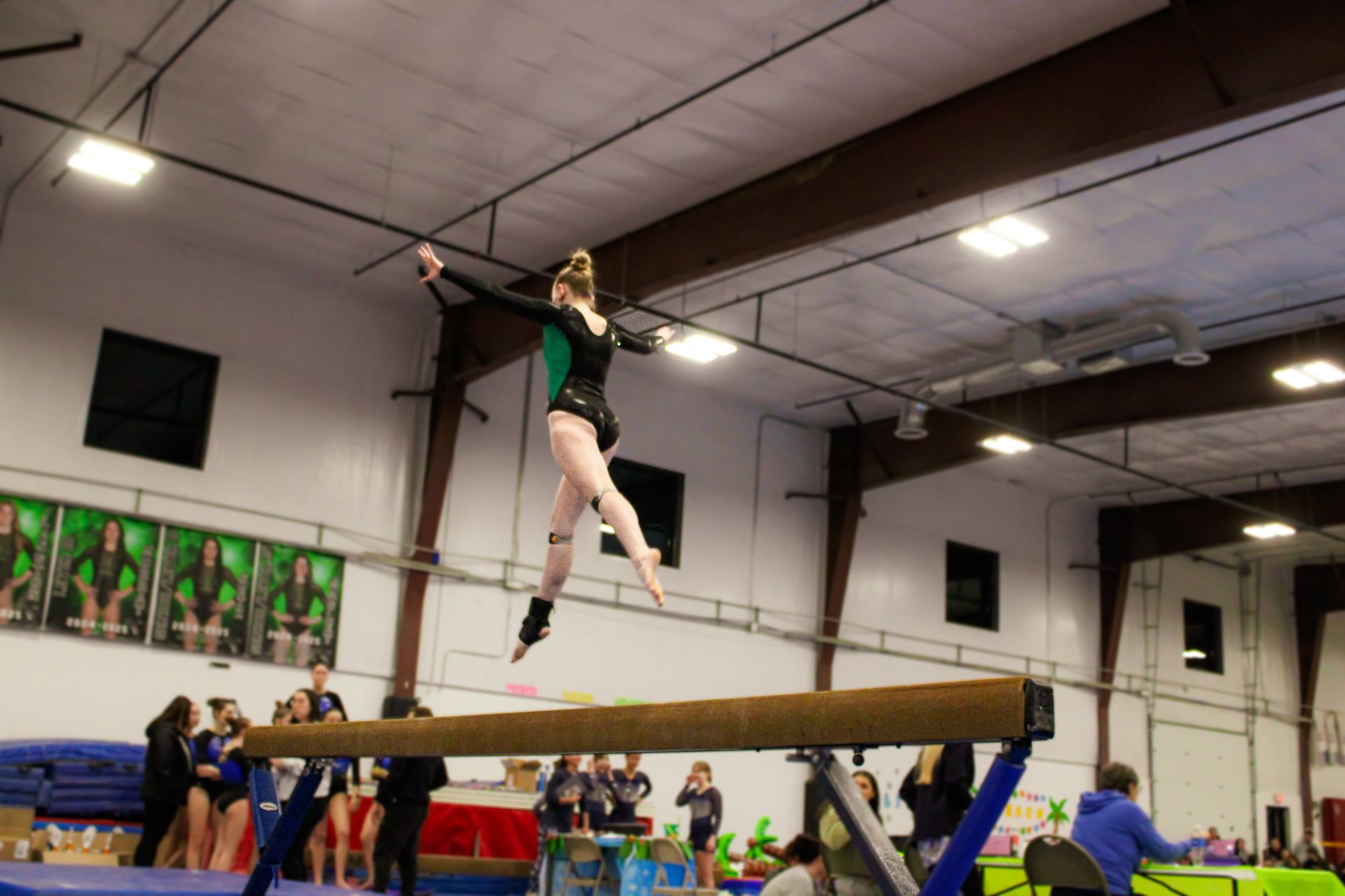 Gymnast balancing on a beam in an indoor gym, with spectators watching below