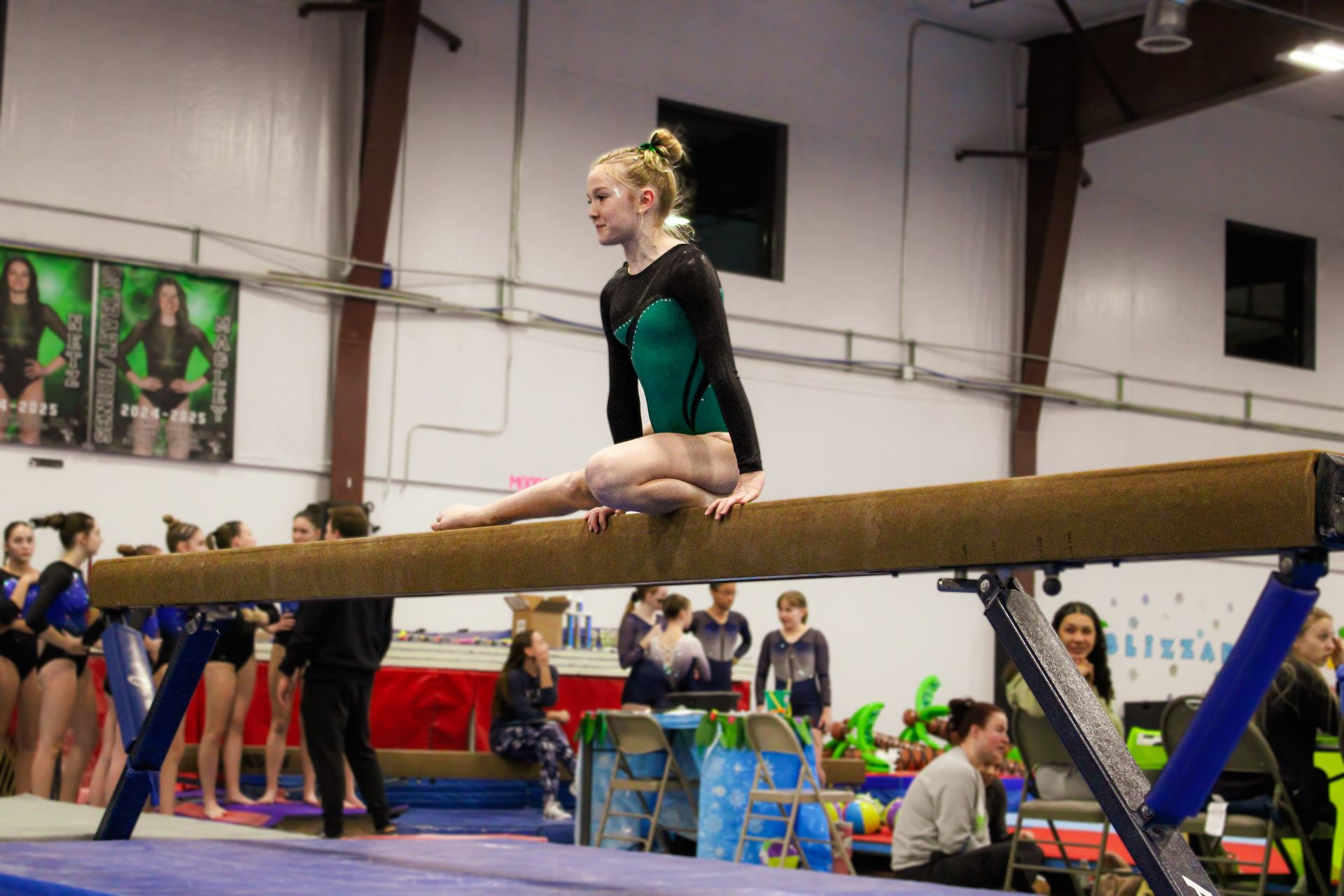 Gymnast balancing on a beam in a gymnasium during a competition, with spectators nearby.