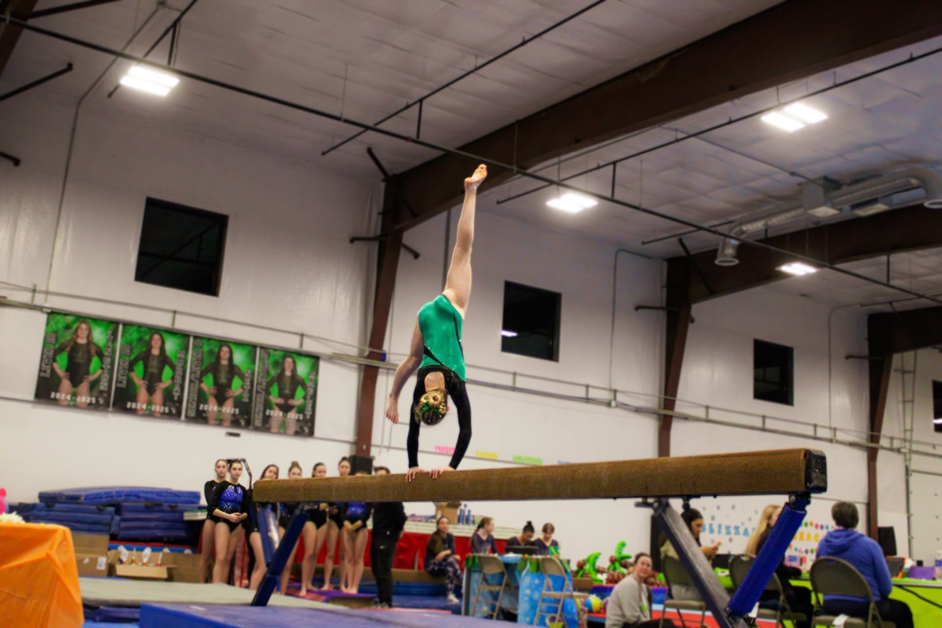 Gymnast balancing upside down on a beam in an indoor gym with teammates watching below