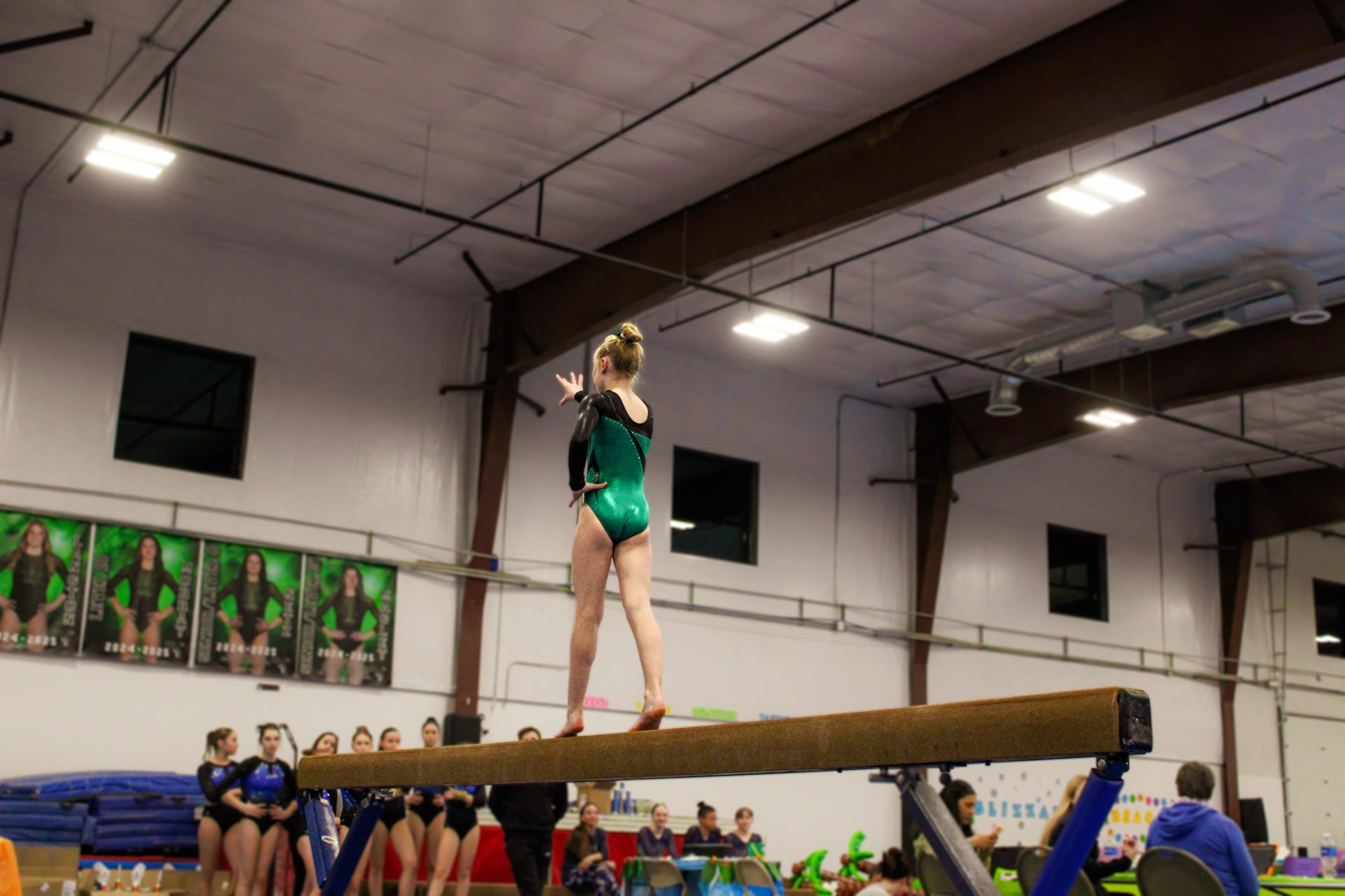 Gymnast balancing on a beam during a competition in a gymnasium, with spectators in the background