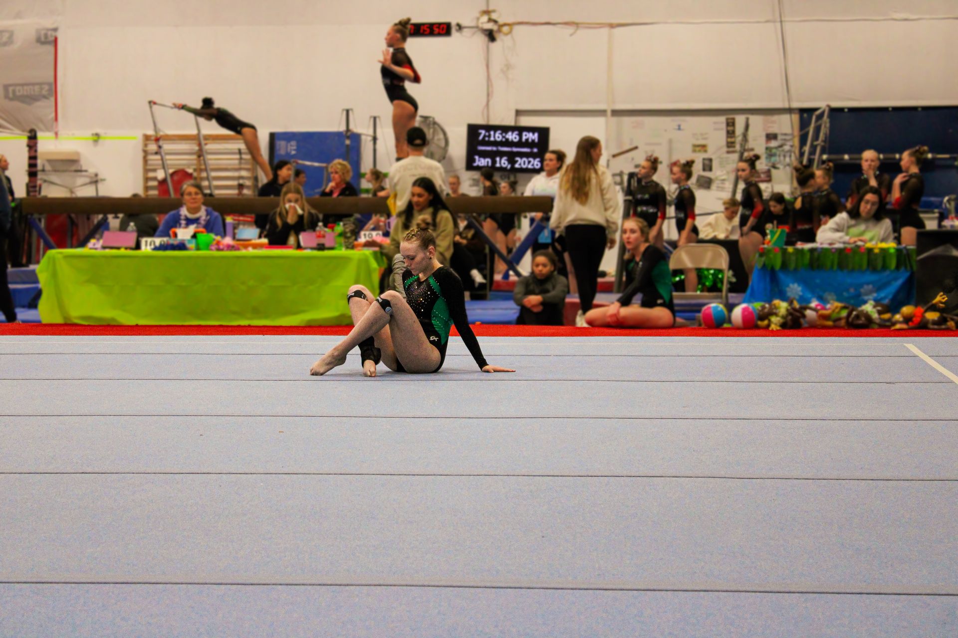 Gymnast posing on a floor mat during a competition, with judges and spectators in the background