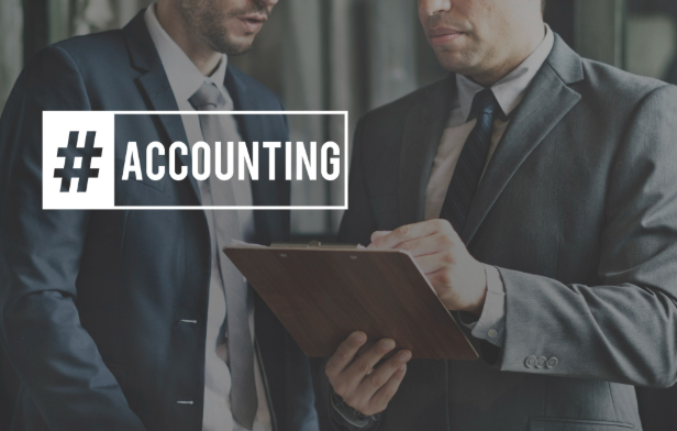 Two professionals review documents, charts, and a calculator at a desk in a bright, sunlit office.