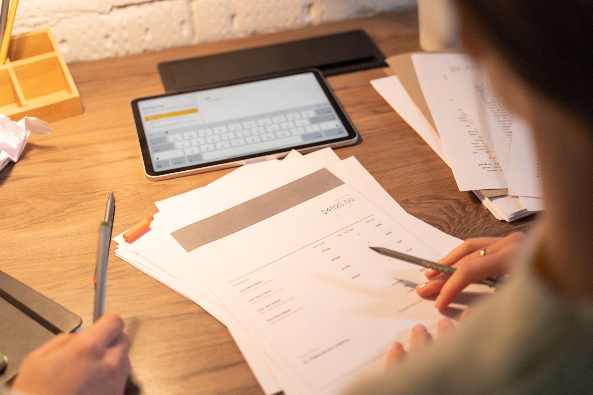 Person working at a desk with papers, a tablet showing a keyboard, and pens. Person working at a desk with papers, a tablet showing a keyboard, and pens.