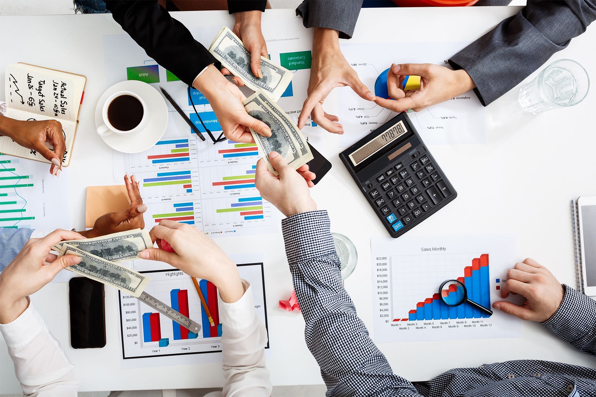 Hands Sharing Money Over a Table With Charts Representing Financial Collaboration Hands Sharing Money Over a Table With Charts Representing Financial Collaboration