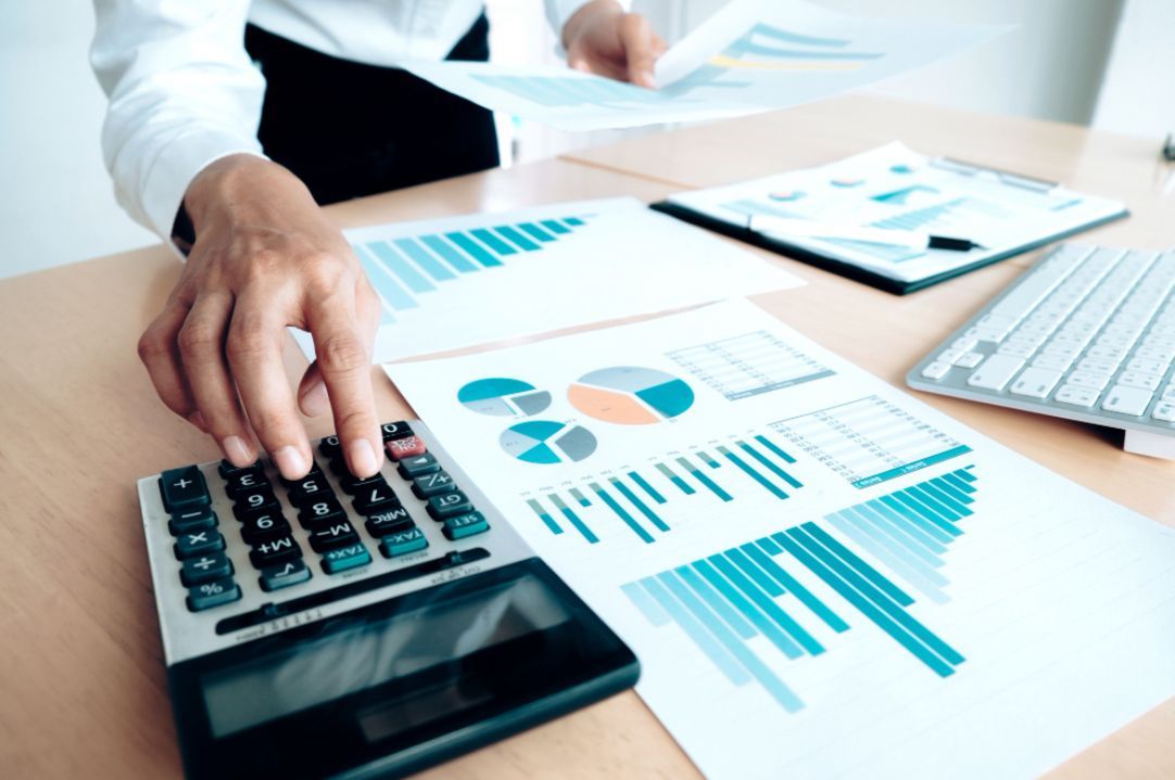Person using a calculator, reviewing charts and graphs on a desk, likely analyzing financial data.