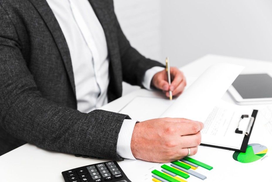 A professional in a suit works at a desk with a calculator, charts, and a tablet, reviewing documents.