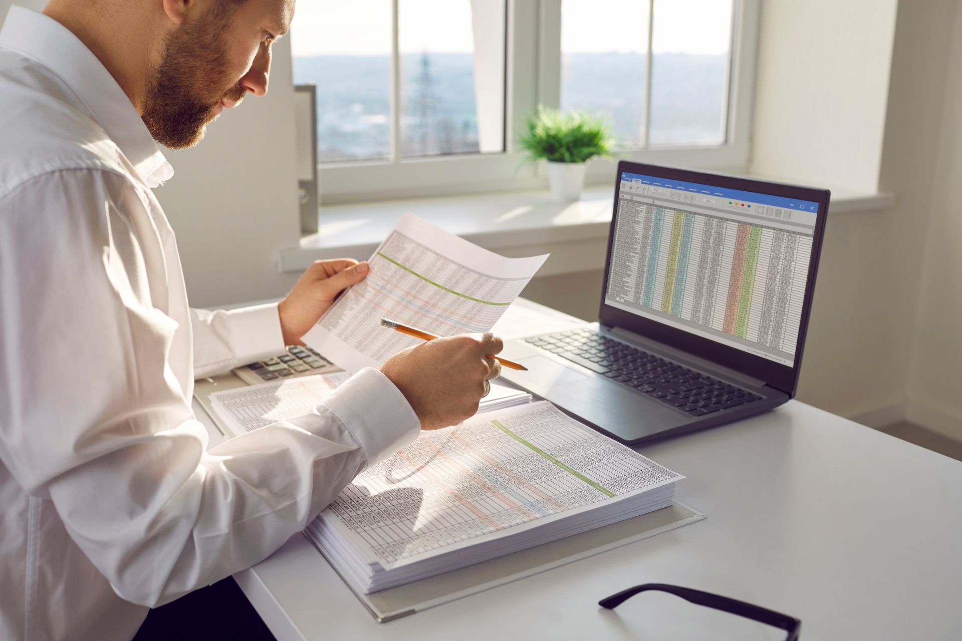 A Man is Sitting at a Desk With a Laptop and a Stack of Papers
