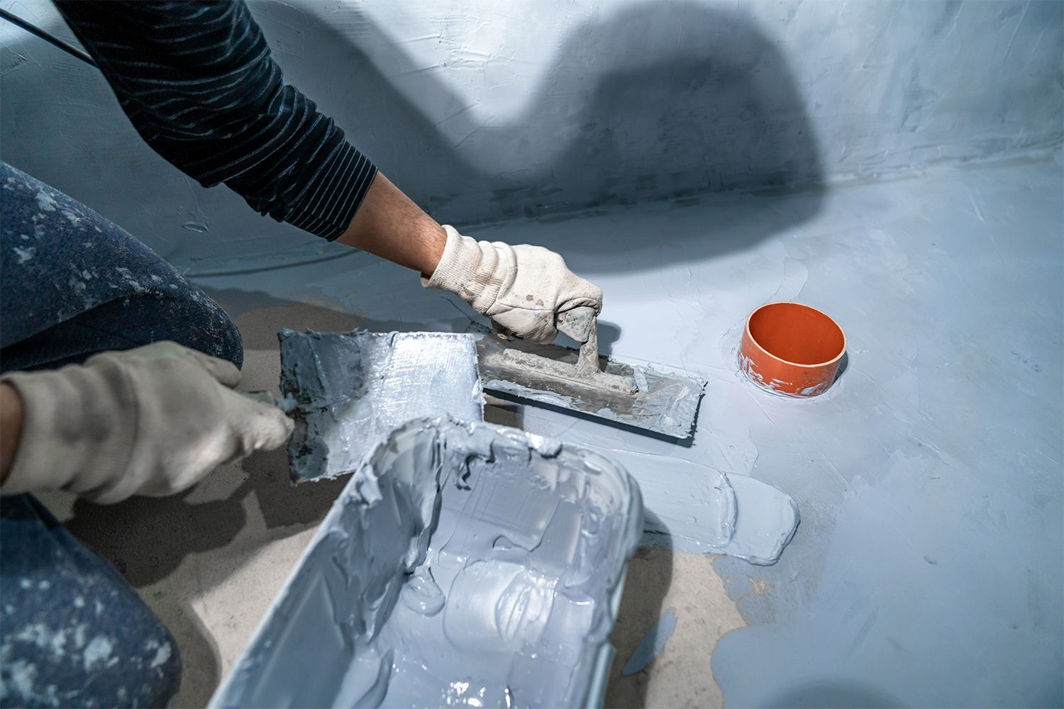 A person is kneeling on the floor applying waterproofing coating.