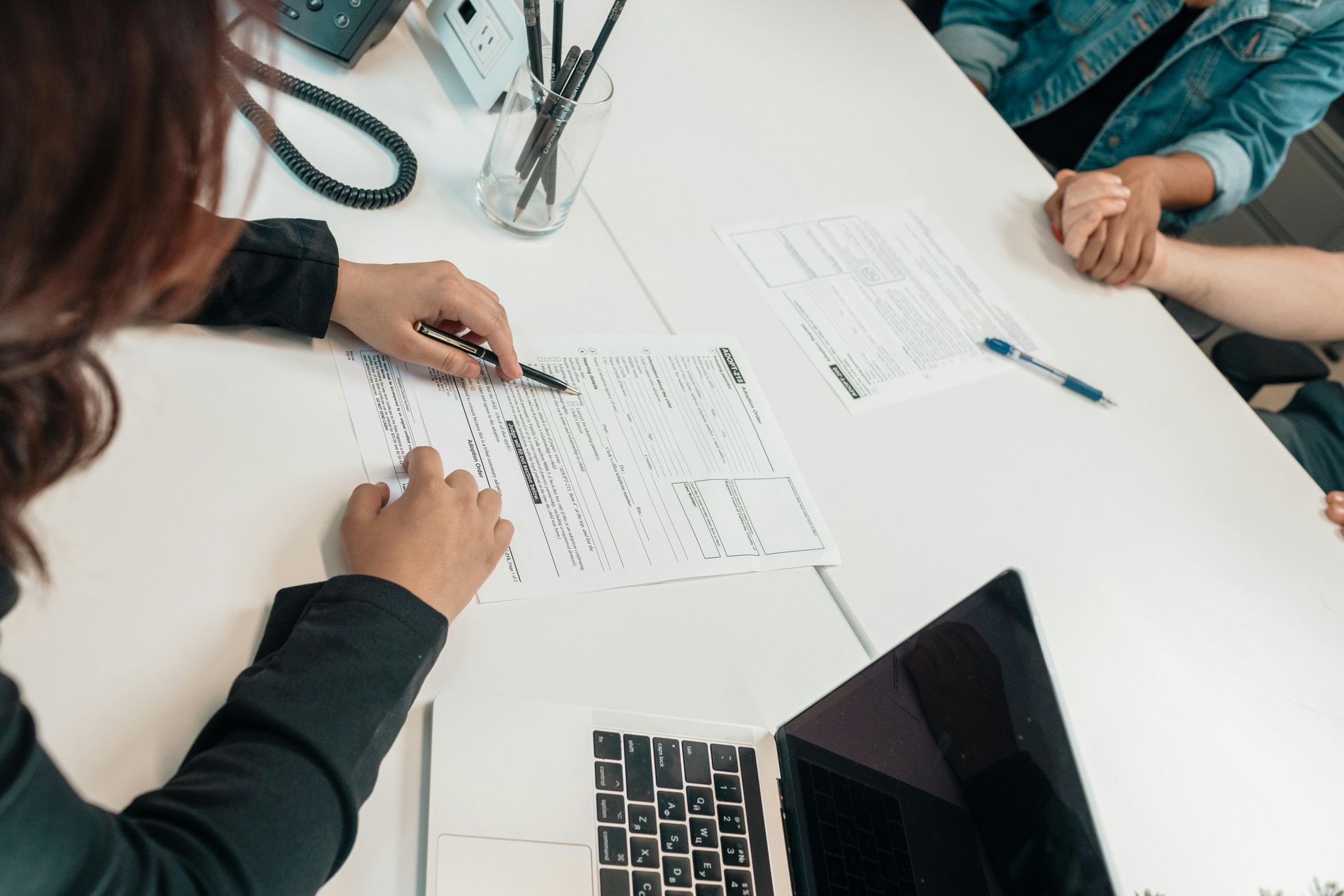People collaborating at a white table, reviewing documents with a pen and a laptop in an office setting.