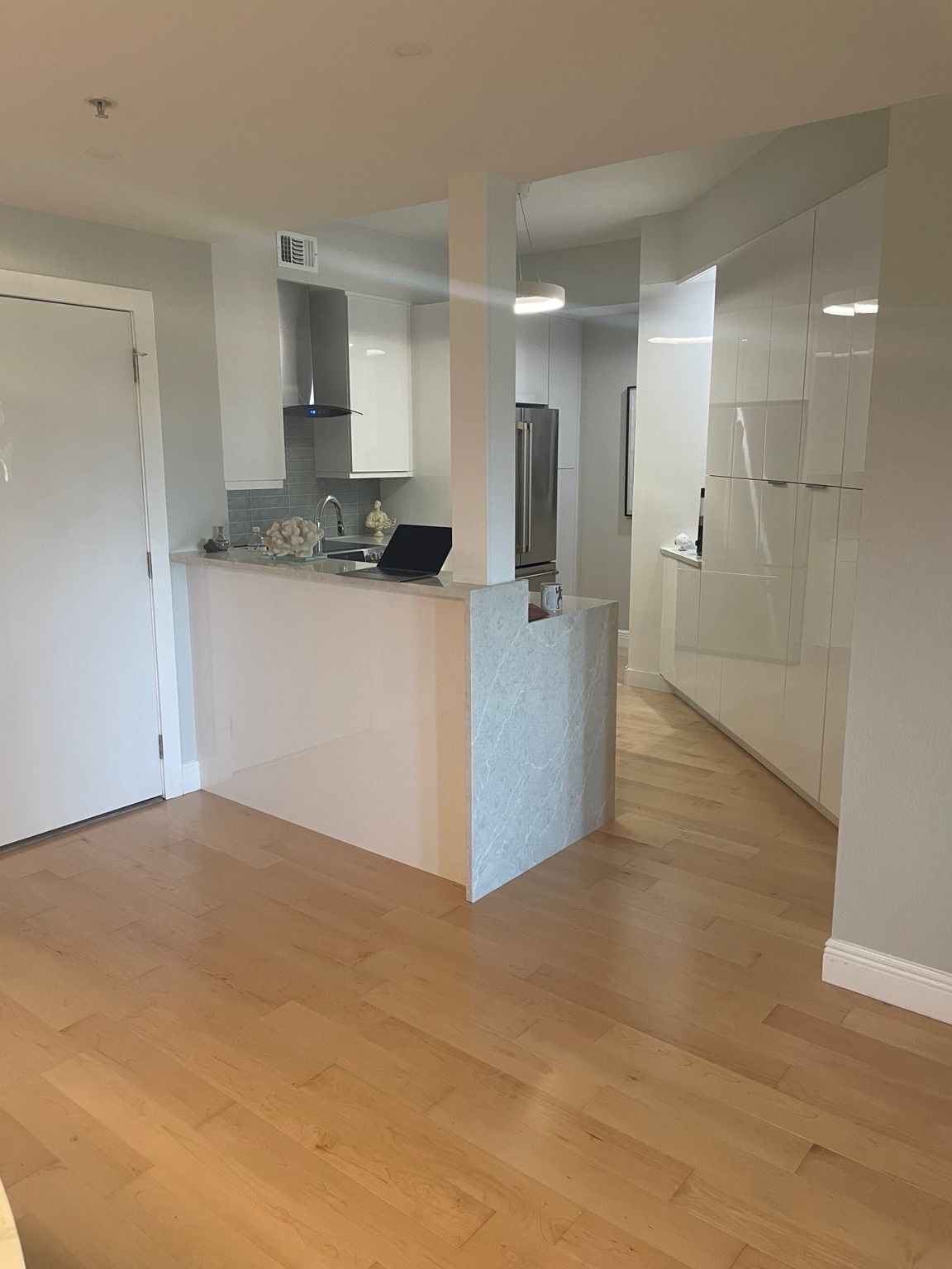 Empty modern kitchen and living area with light wood floors, white walls, and a small breakfast bar.