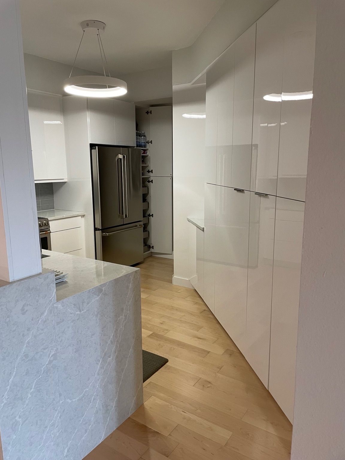 Modern white kitchen with stainless steel fridge, light wood floor, and granite island.