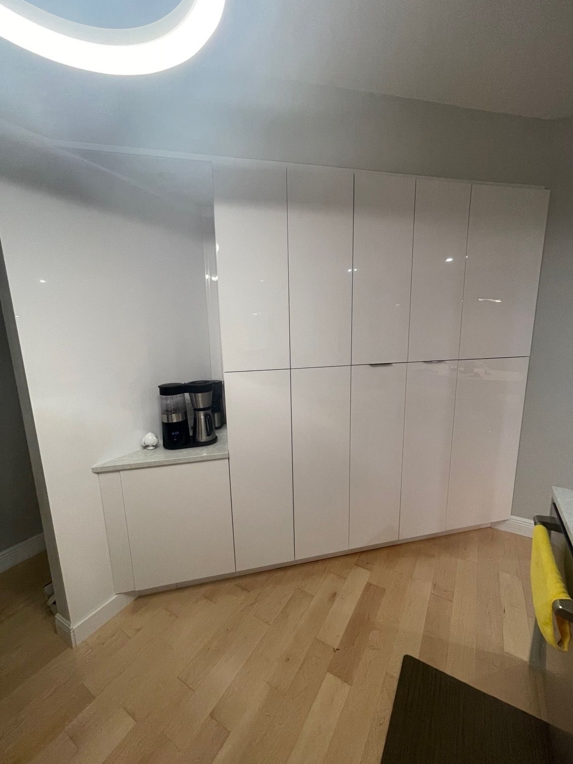 Modern white built-in cabinets in a bright room with a light wood floor and coffee maker on a counter