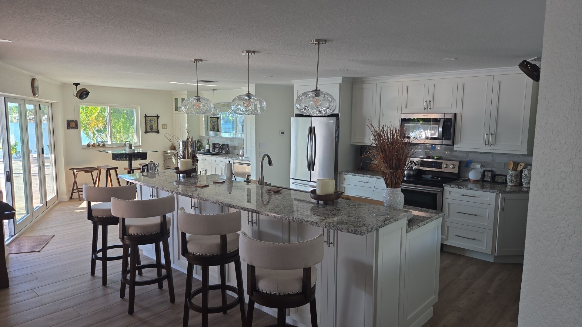 Spacious white kitchen with island, seating, and appliances. Large windows and pendant lights.