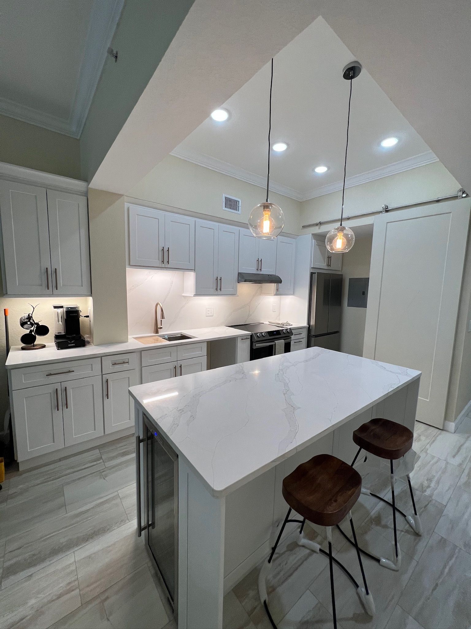 Modern white kitchen with vaulted ceiling, central island, pendant lights, and two stools