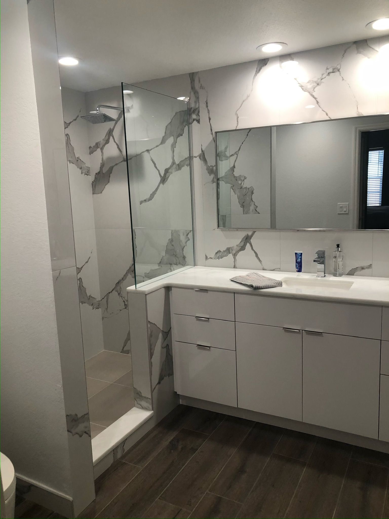 Modern bathroom with marble-patterned walls, large mirror, white vanity, and dark wood flooring