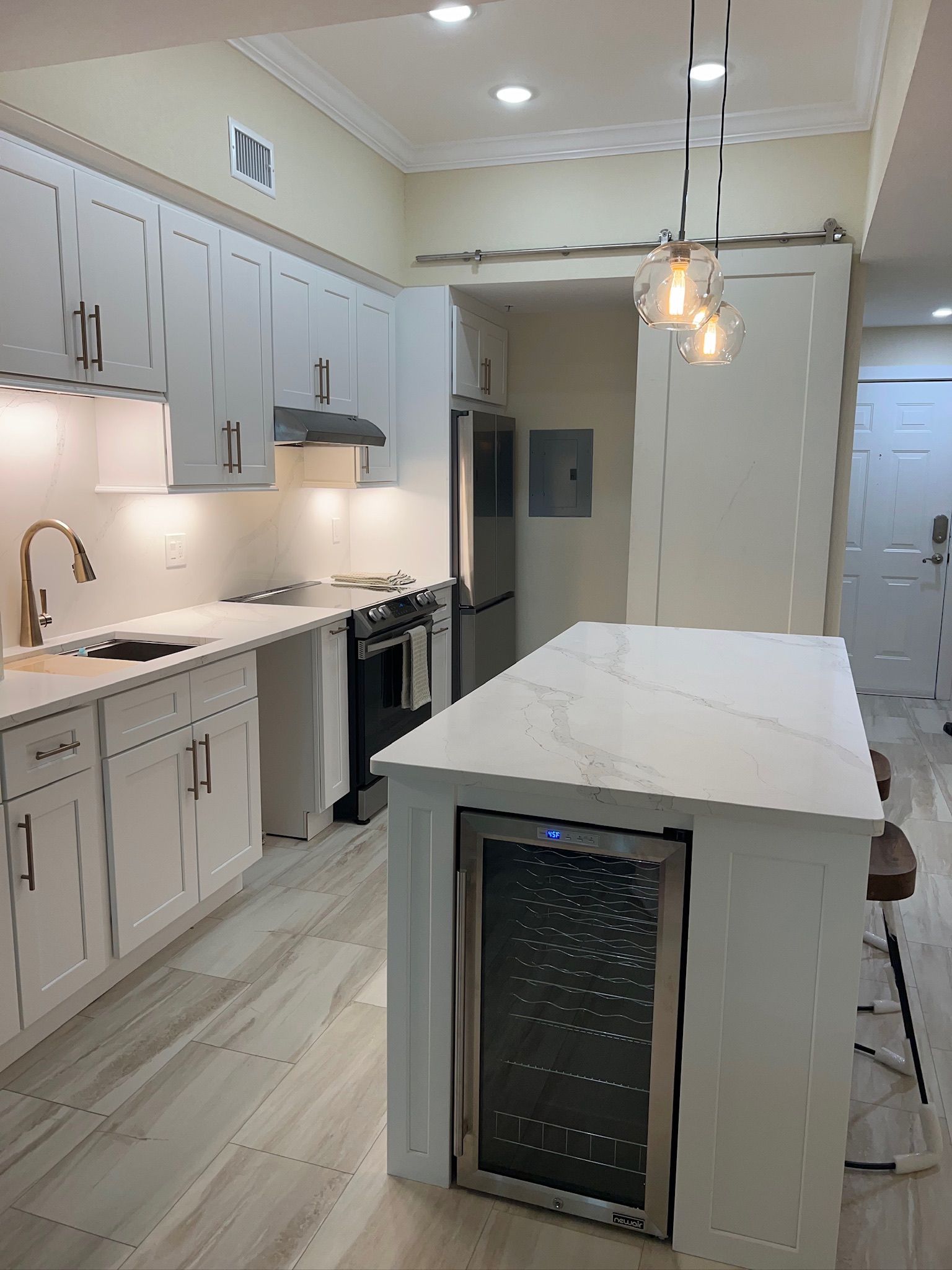 Bright modern kitchen with white cabinets, marble island, stainless appliances, and pendant lights