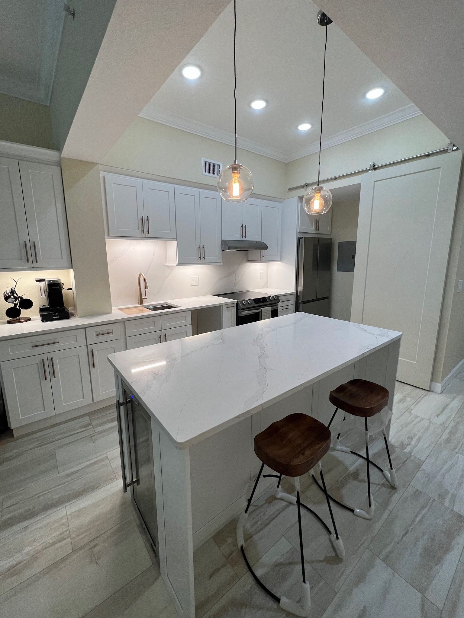 Modern white kitchen with island, pendant lights, built-in cabinets, and two stools