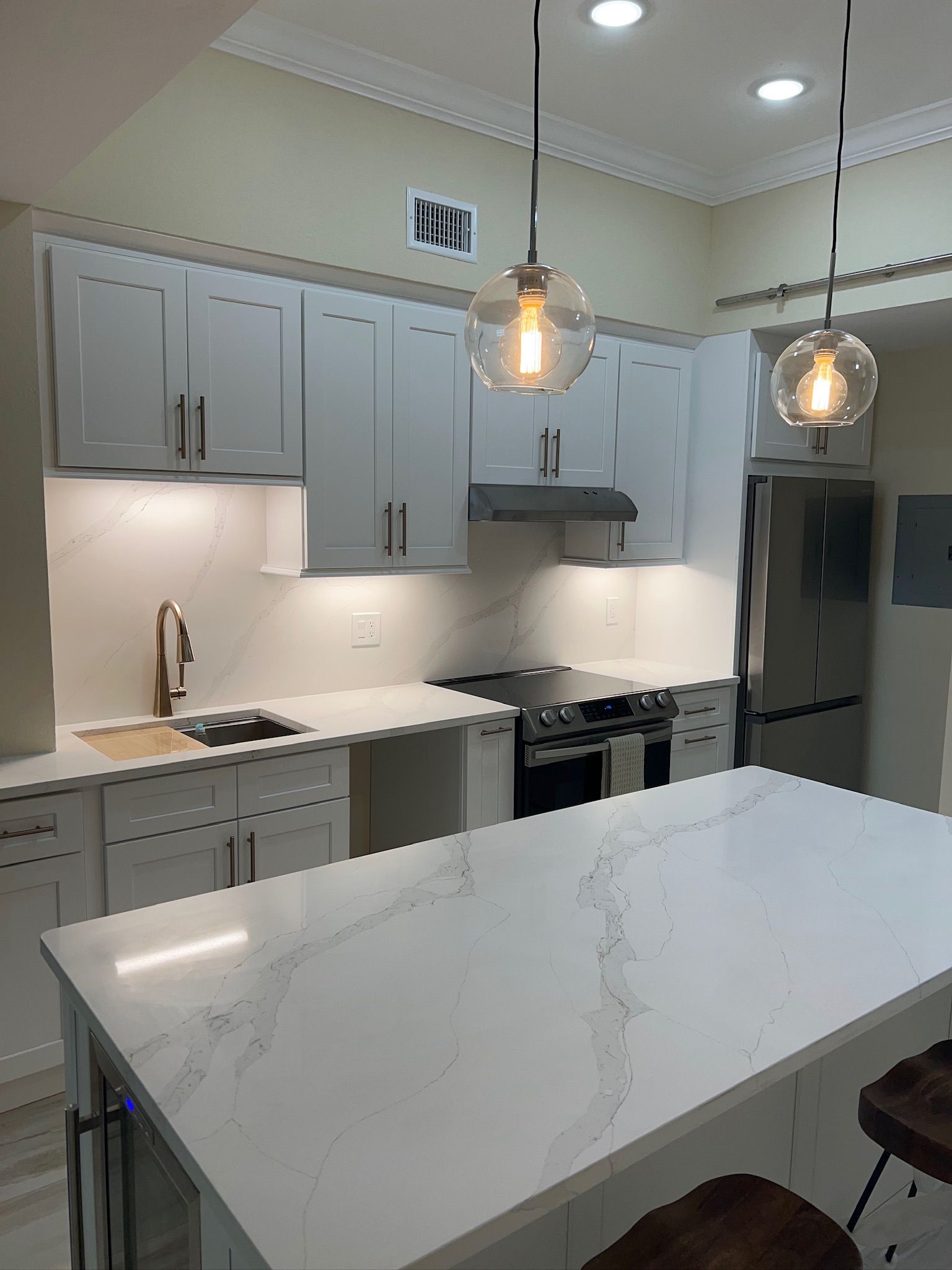 Bright modern kitchen with white cabinets, marble island, pendant lights, and stainless steel appliances