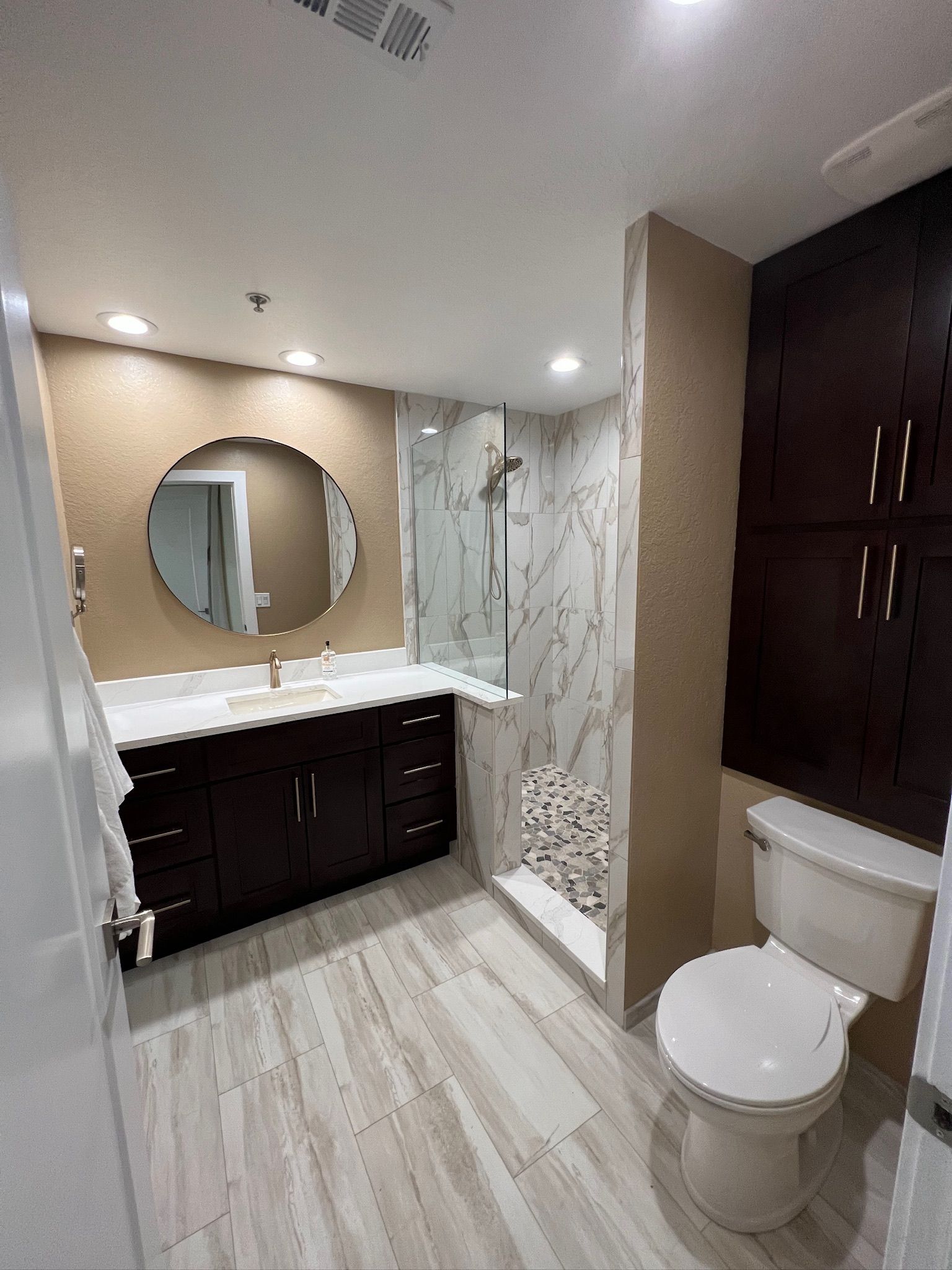 Modern bathroom with double vanity, round mirror, shower, and toilet in neutral tones